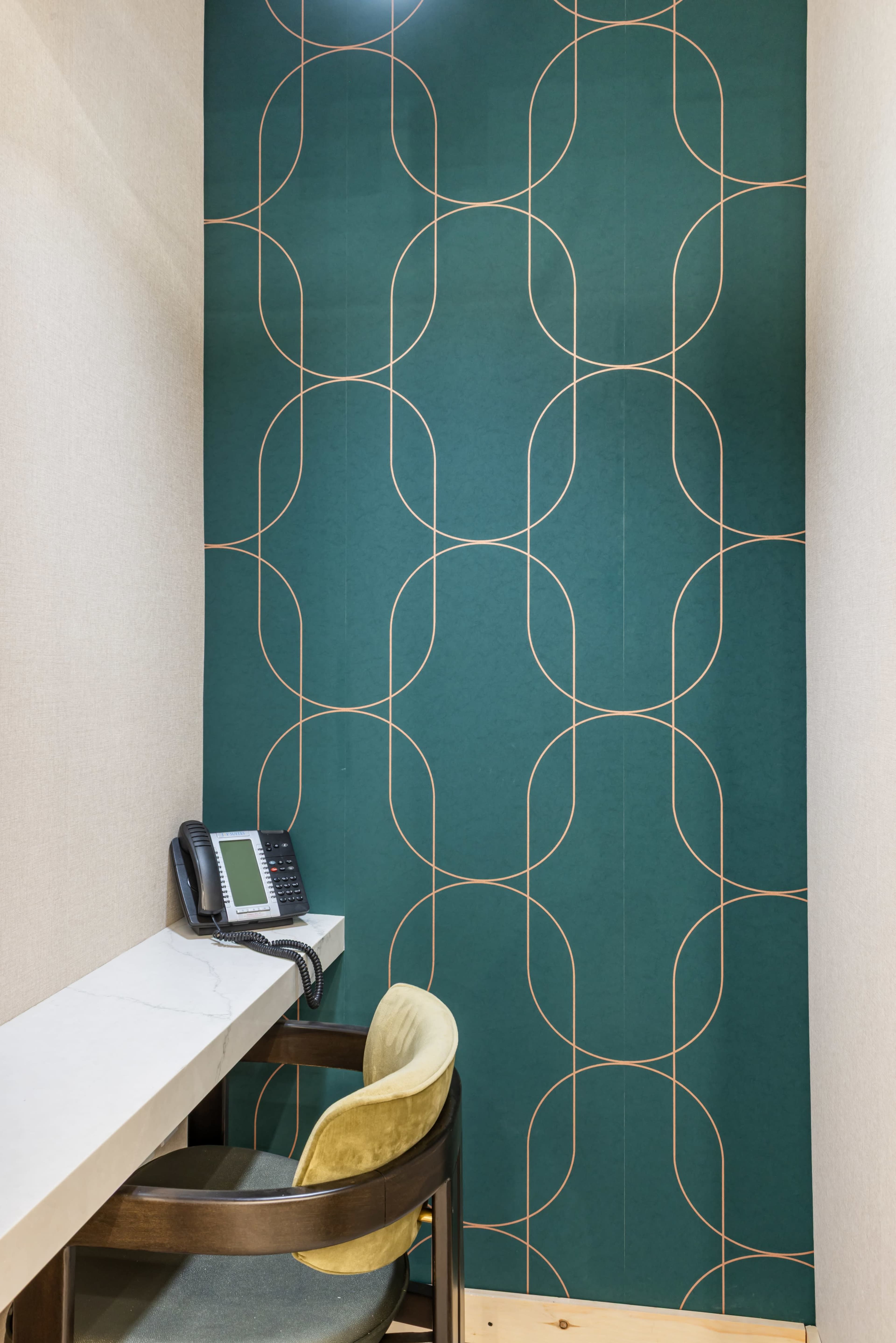 The image shows a small office corner featuring a marble-topped desk, a phone, and a chair against a patterned teal wall.