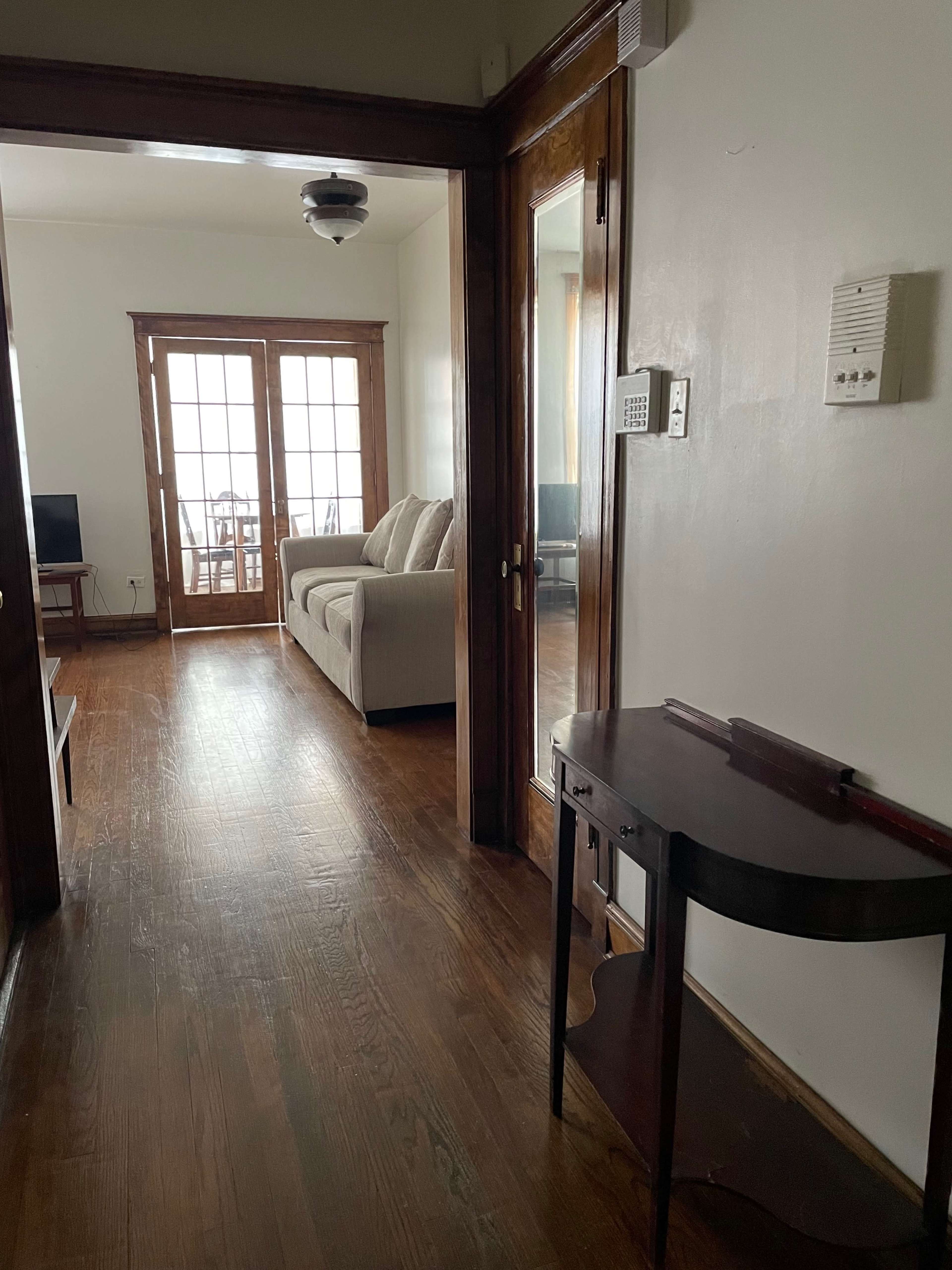 A hallway leading to a living room with a couch and dining area visible through a set of French doors.