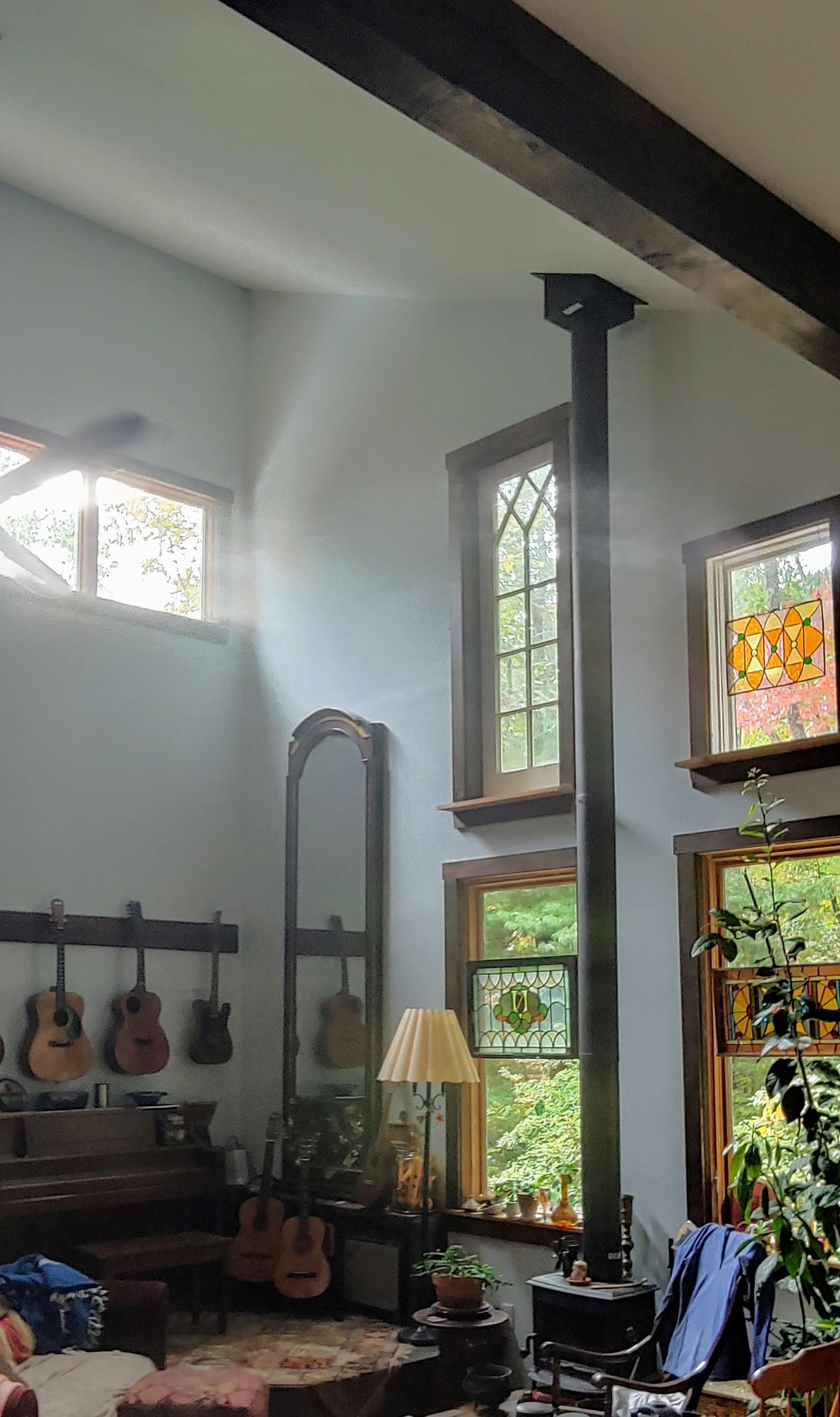 A sunbeam streams through the stained glass windows of a living room filled with a piano, guitars, and plants.