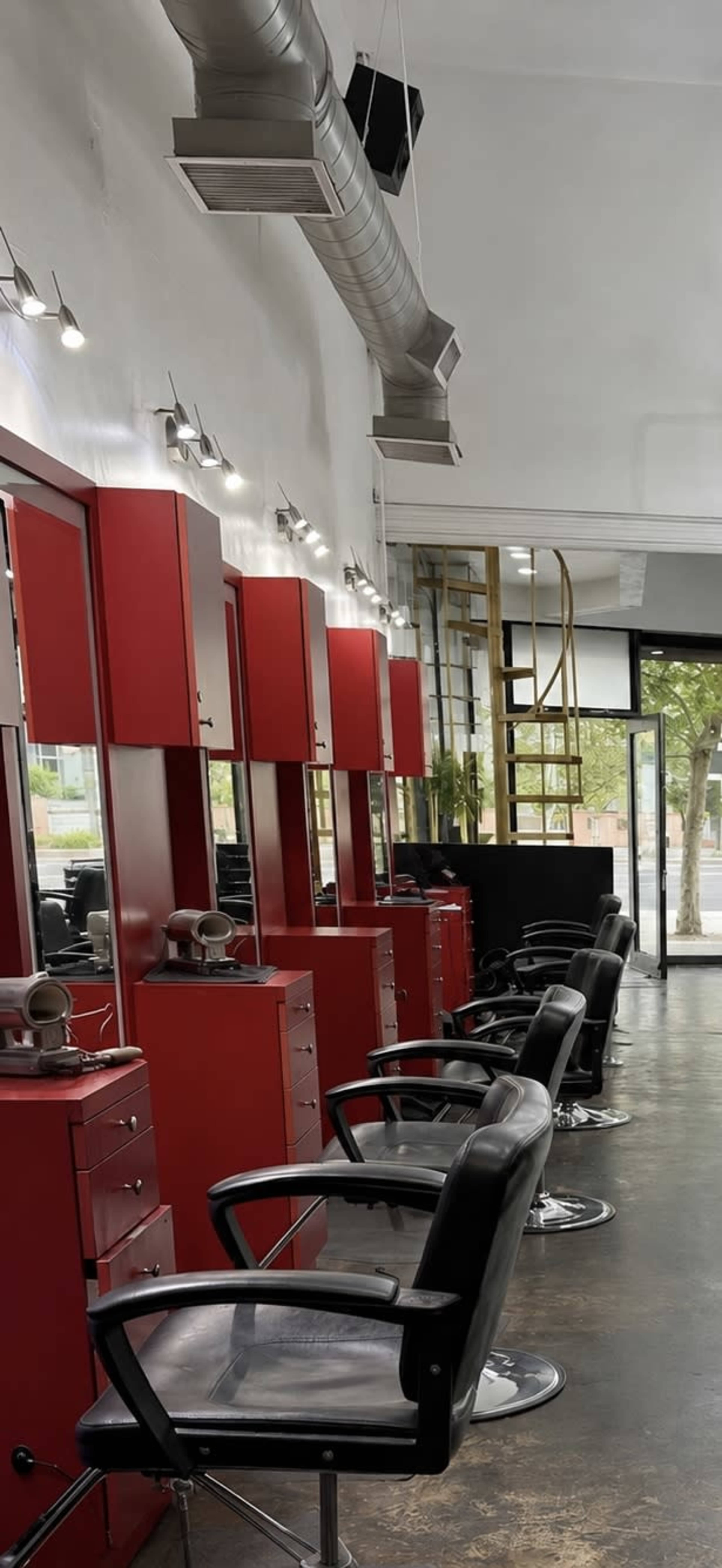 The image shows a modern hair salon with red cabinets, black chairs, and large mirrors lined up along one wall.