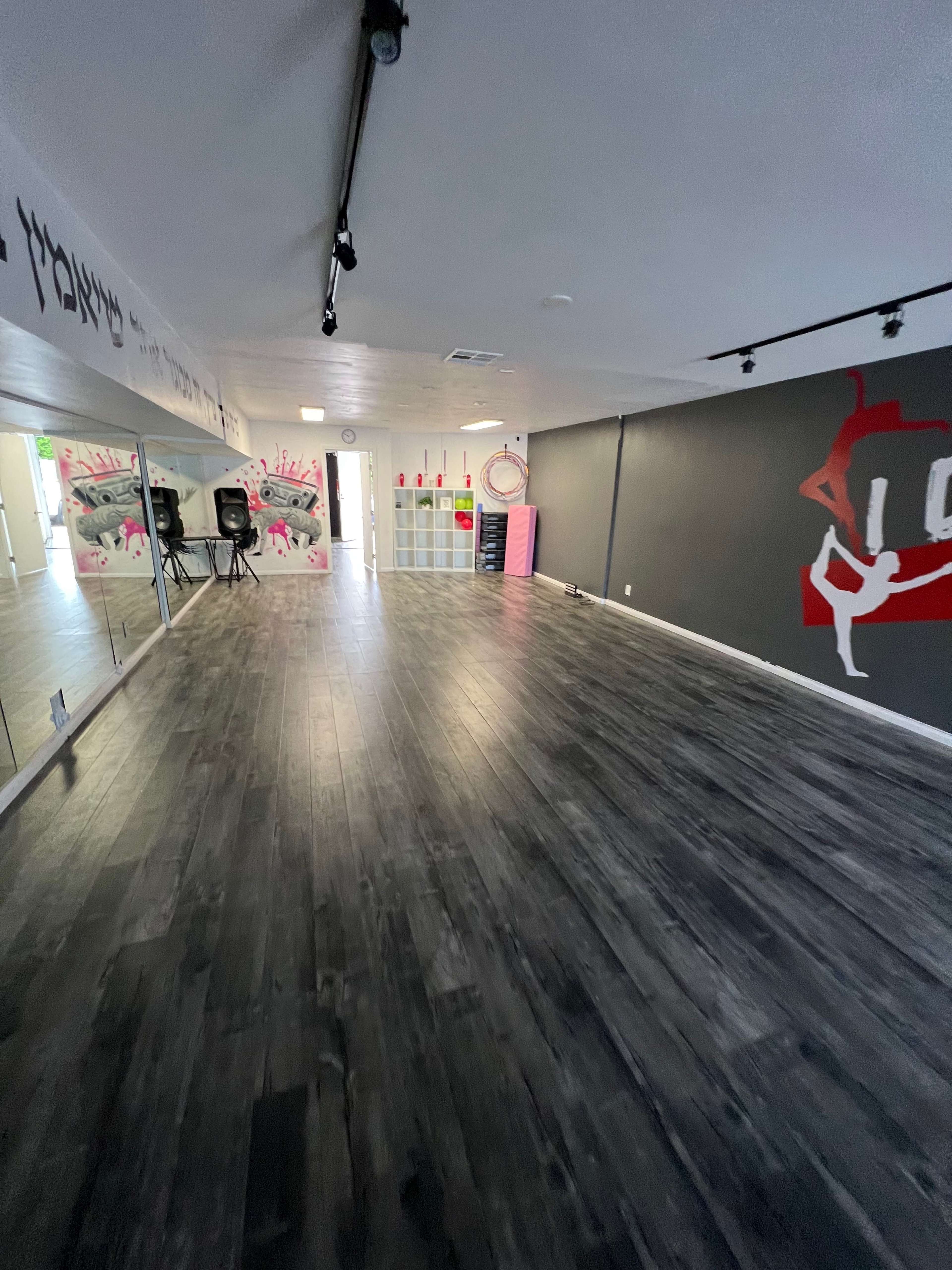 An empty dance studio with a mirrored wall, wooden flooring, and graffiti-style artwork on the walls.