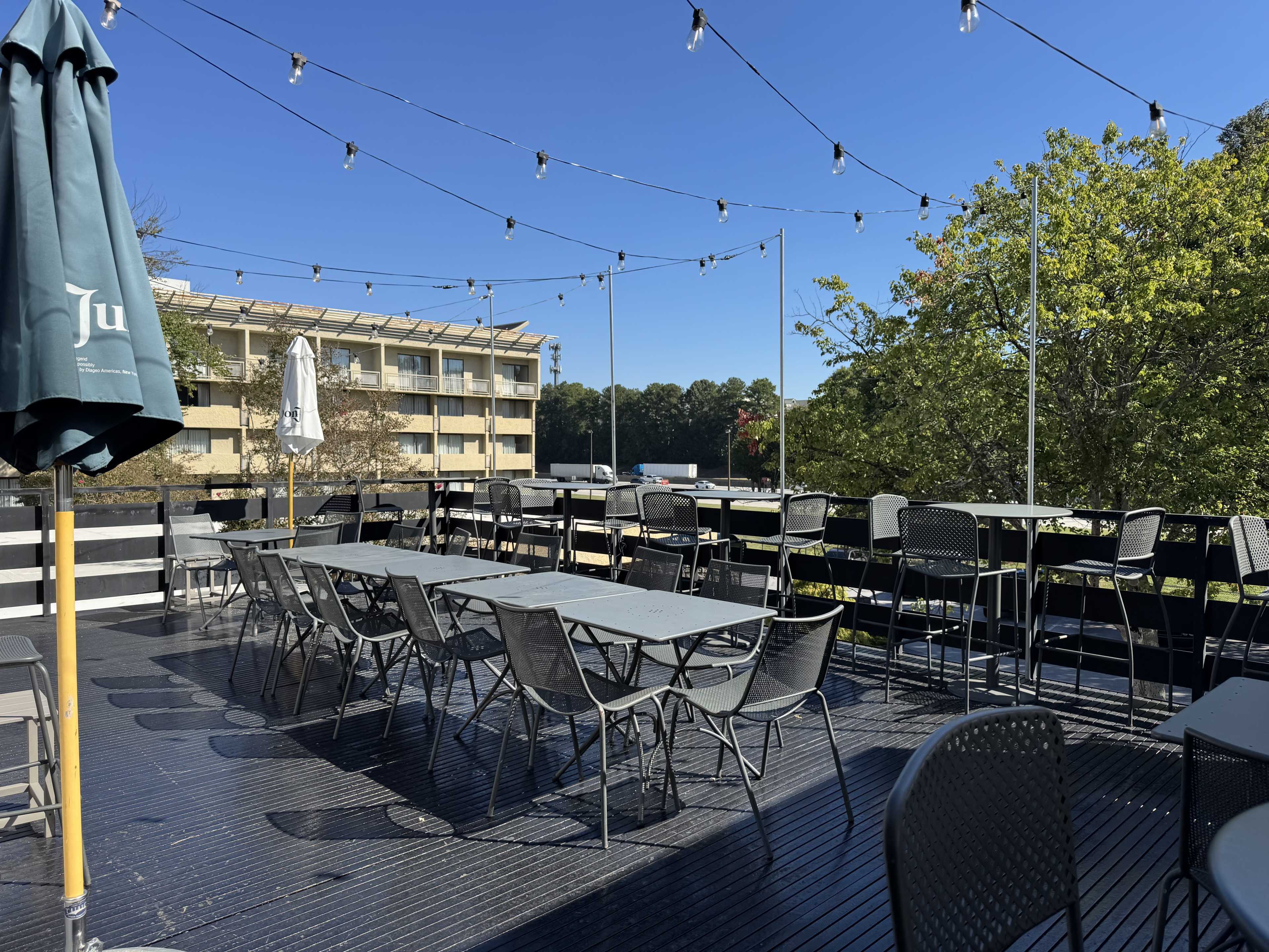 The image shows a rooftop terrace with multiple tables and chairs, string lights overhead, and a building in the background.