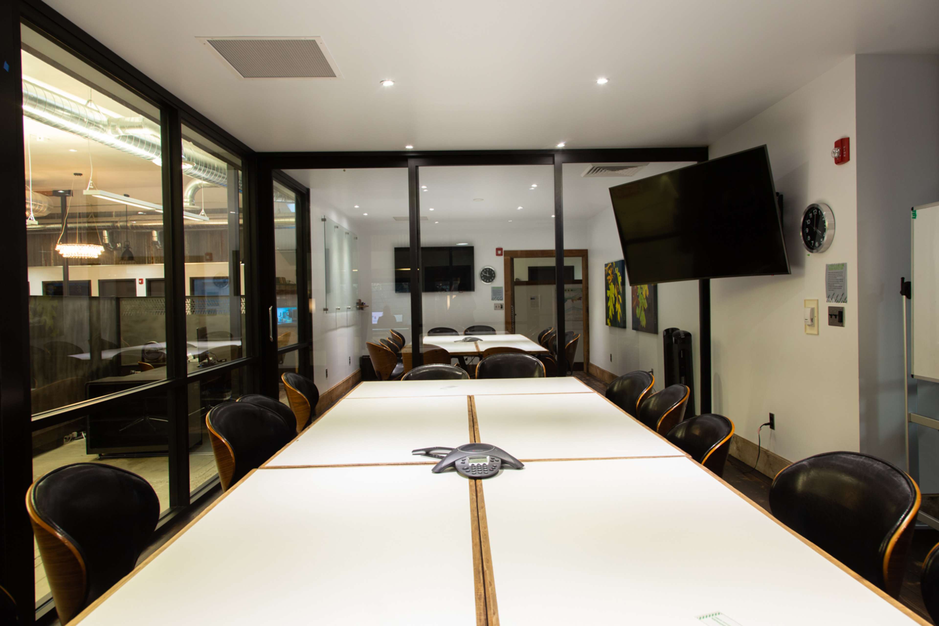 A modern conference room features a long table with black chairs, a large screen on the wall, and glass partitions.