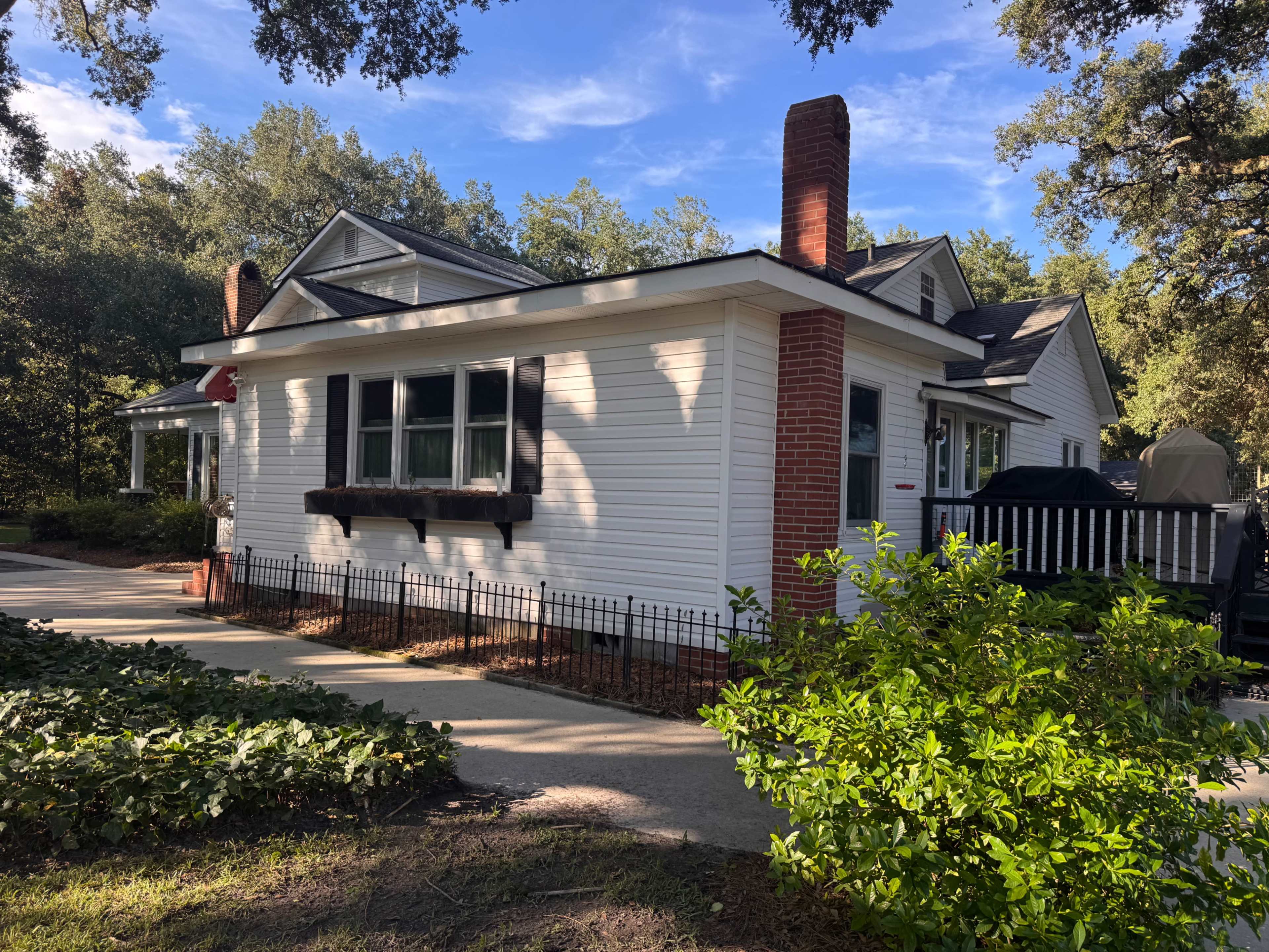 A single-story, white house with a front porch and red brick chimneys is surrounded by greenery and a walkway.