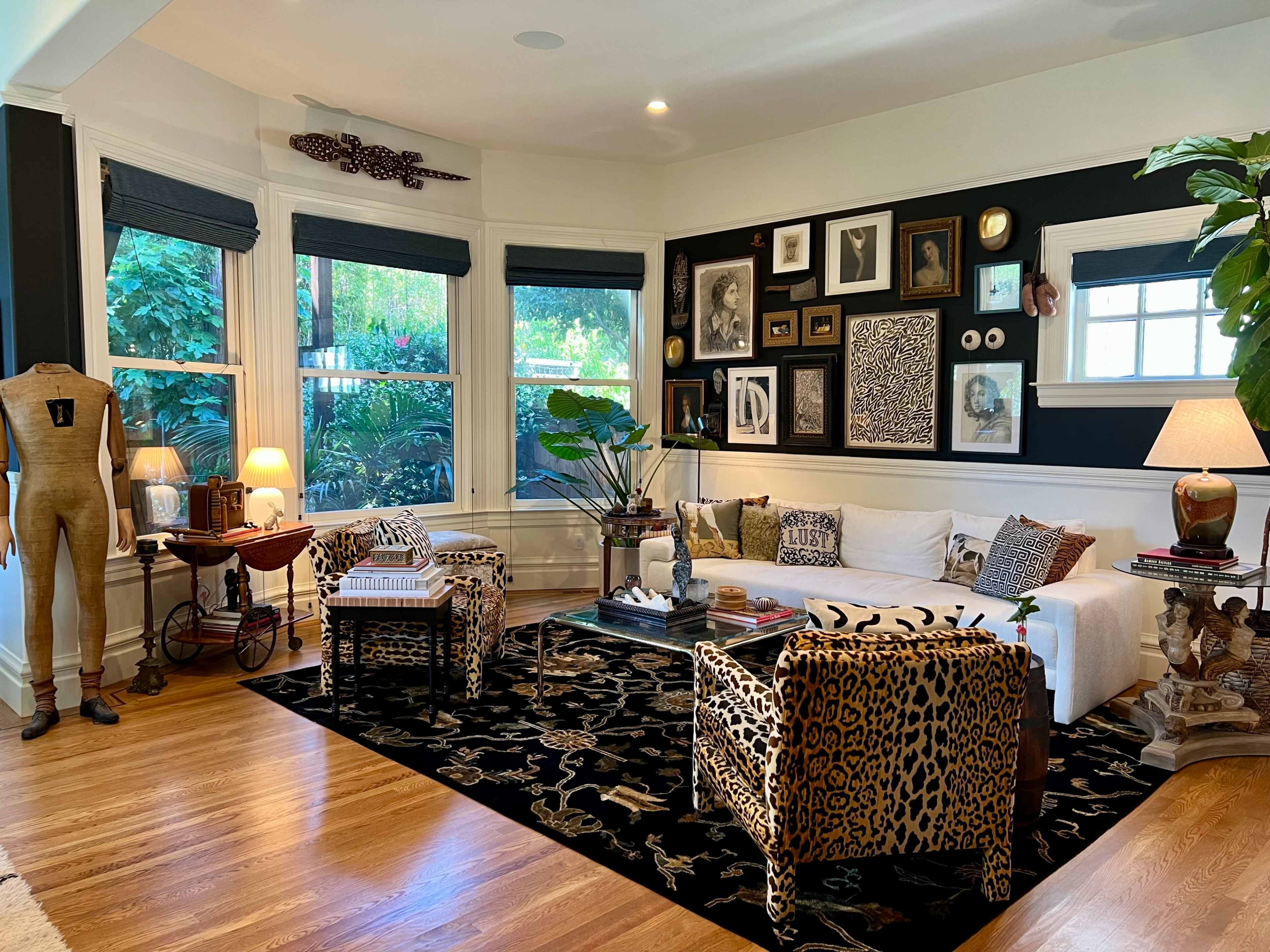 A stylish living room with a white sofa, leopard-print chairs, a black and gold patterned rug, and an eclectic wall display of framed art and photographs.