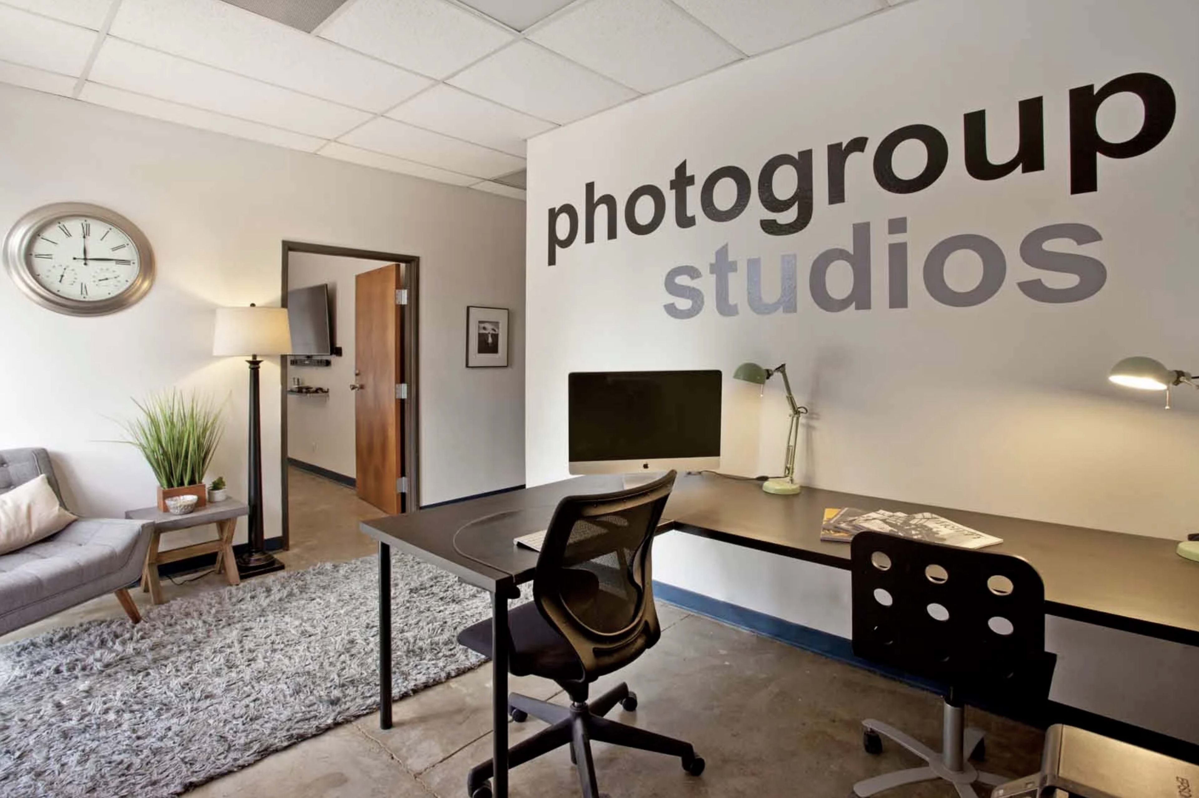 A modern office space with a desk, a computer, a lamp, and a large wall displaying the text "photogroup studios."