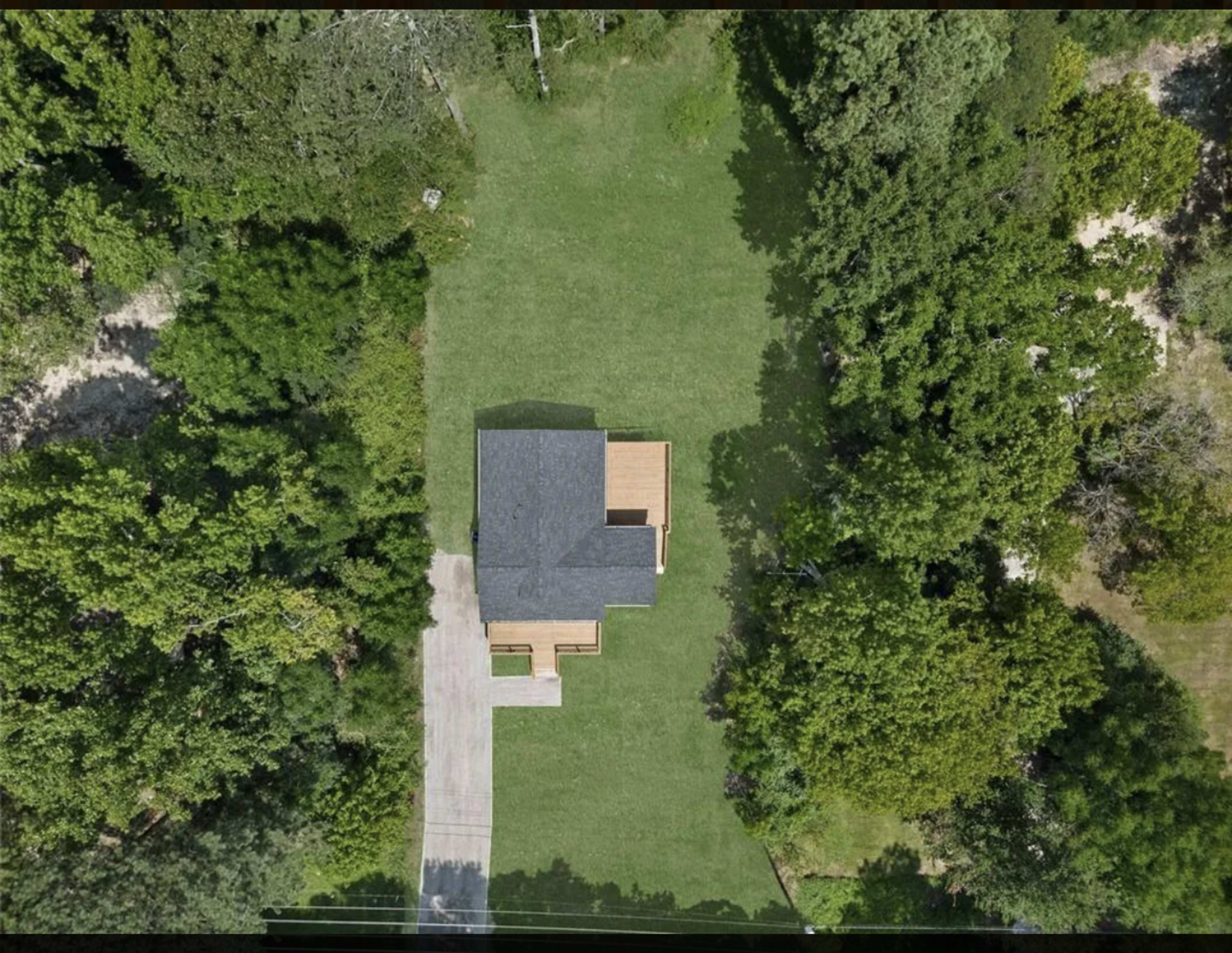 An aerial view of a house situated on a green lawn surrounded by dense trees.