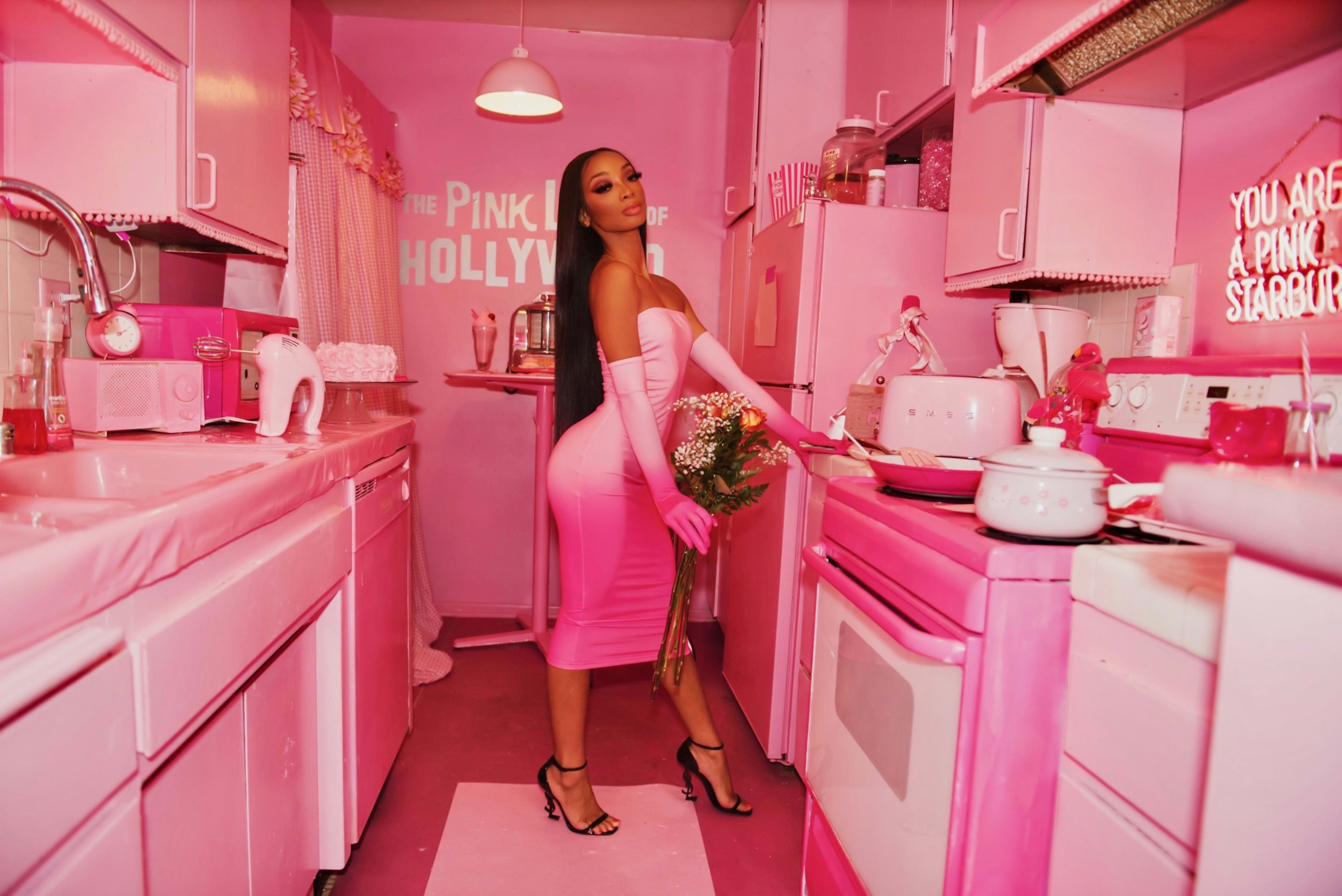 Une femme dans une cuisine rose avec des appareils roses lors d'un shooting photo hollywoodien.