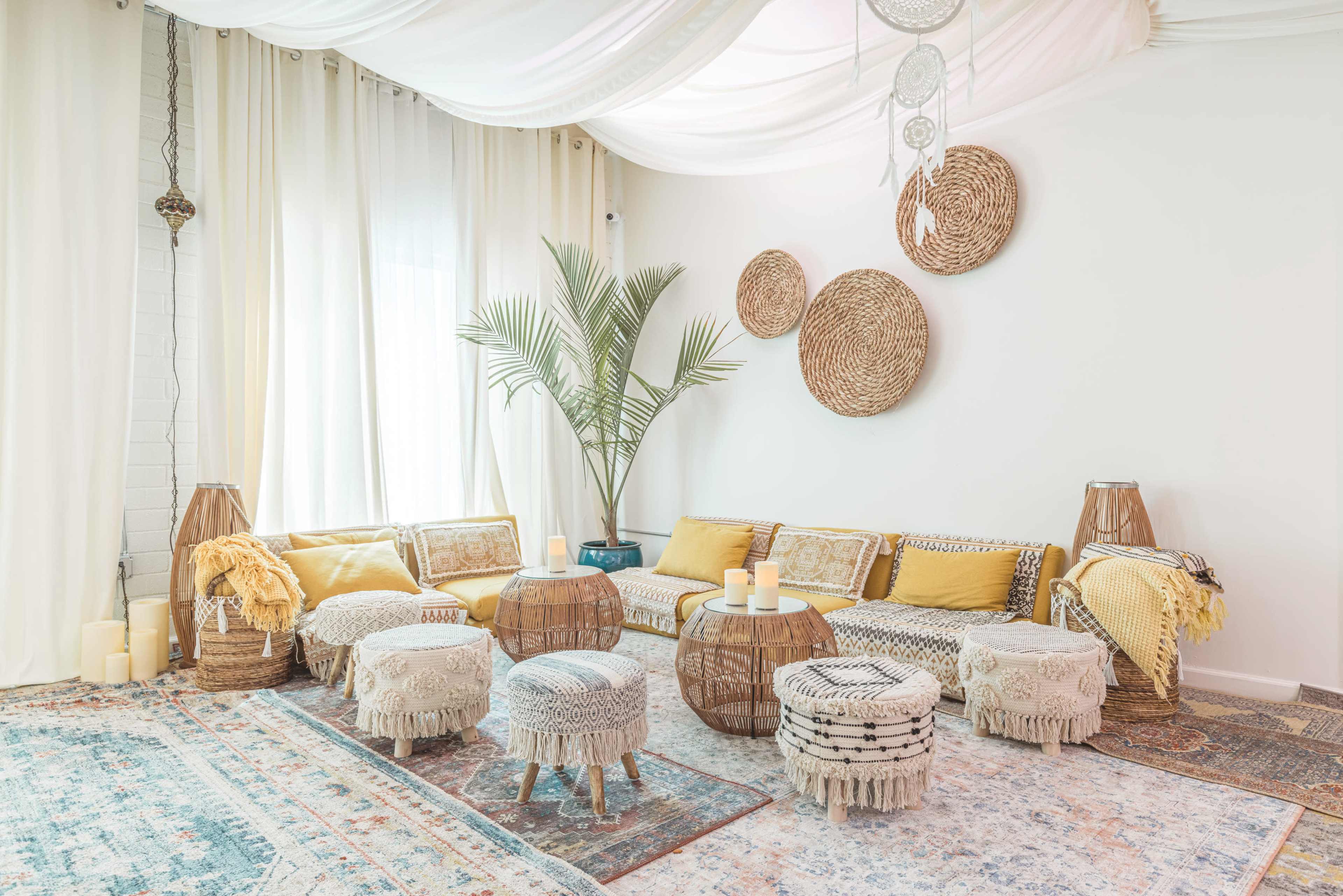 A cozy living room with a large, U-shaped sofa adorned with yellow and neutral cushions, surrounded by woven furniture, decorative rugs, and illuminated candles.