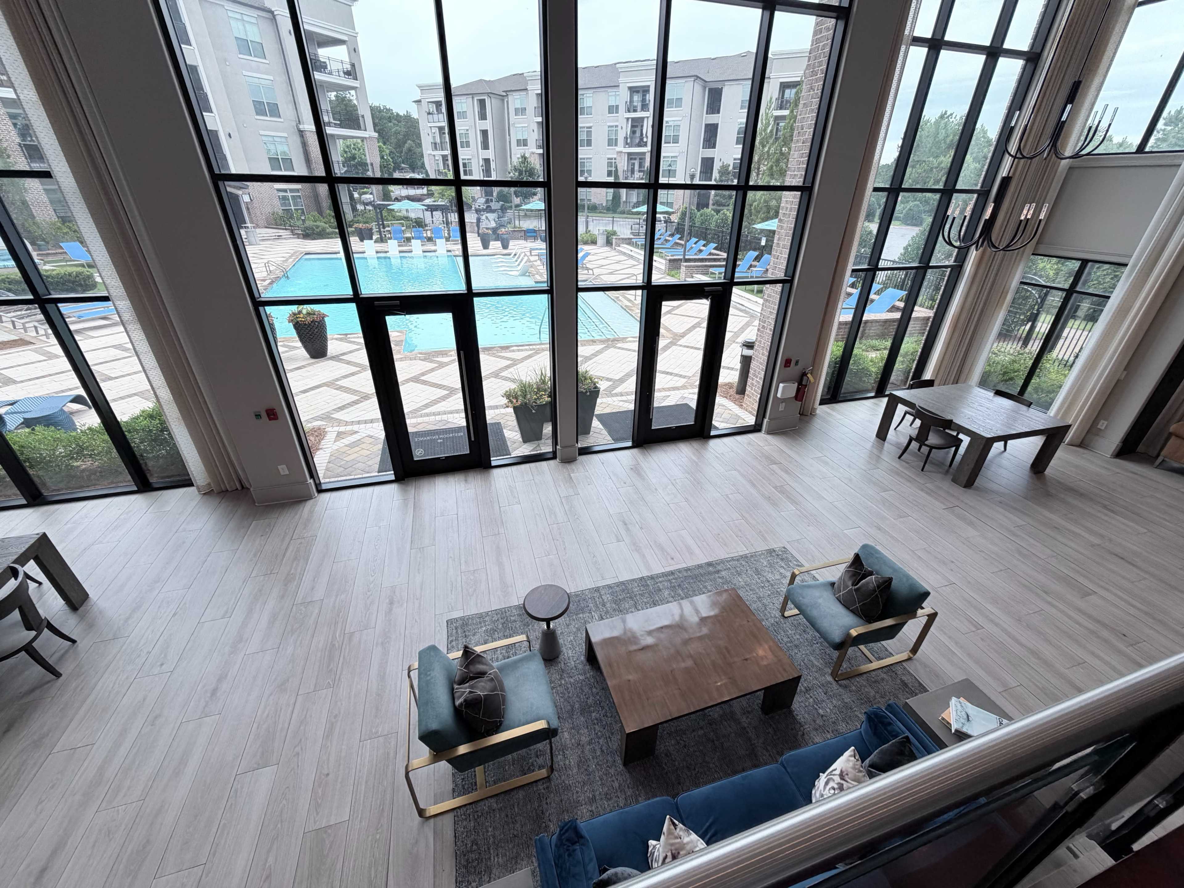 The image shows a spacious indoor lounge area with large windows overlooking a pool and patio area.