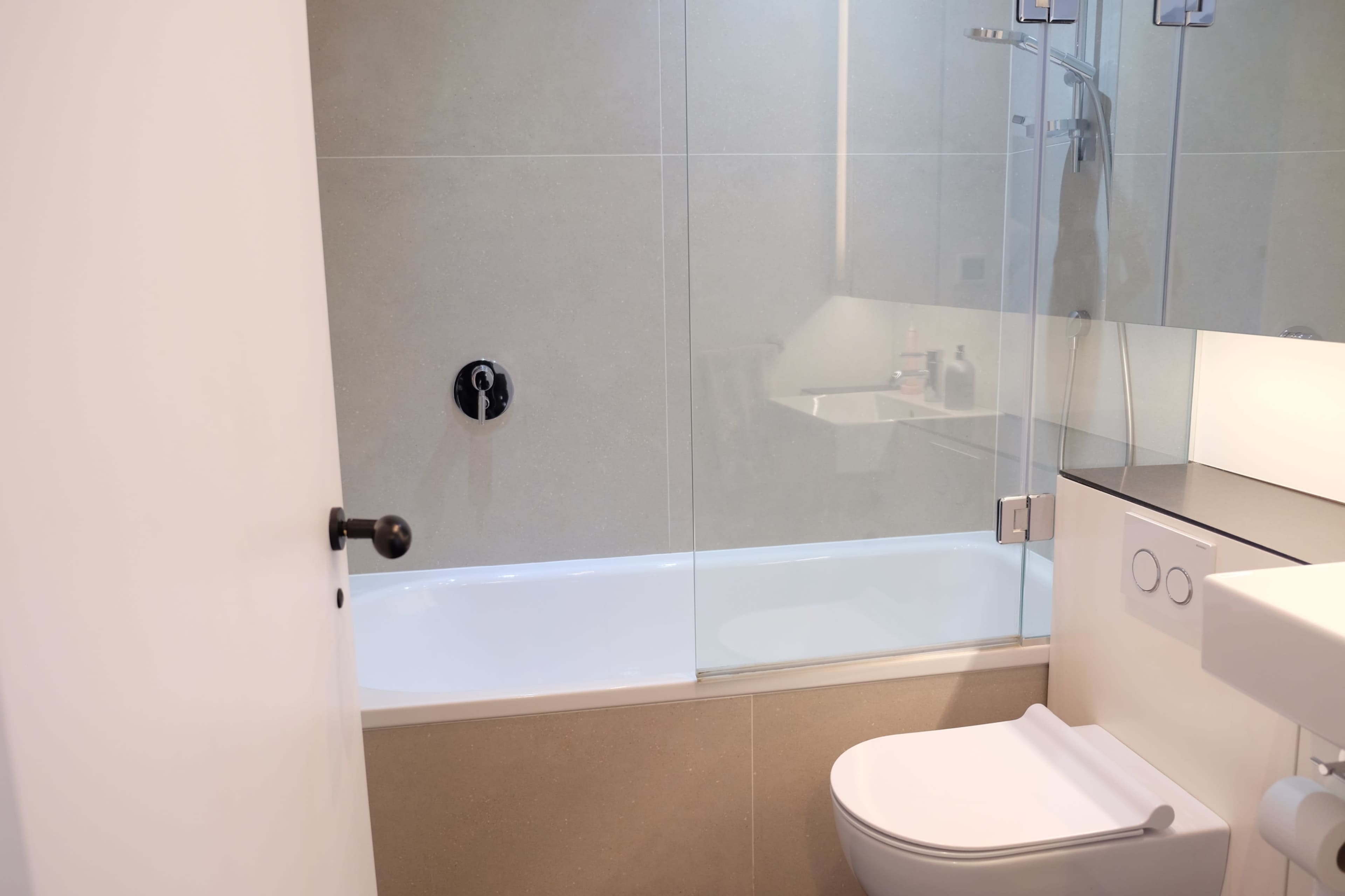 A clean bathroom with a glass-enclosed bathtub, toilet, and a large mirror reflecting the space.