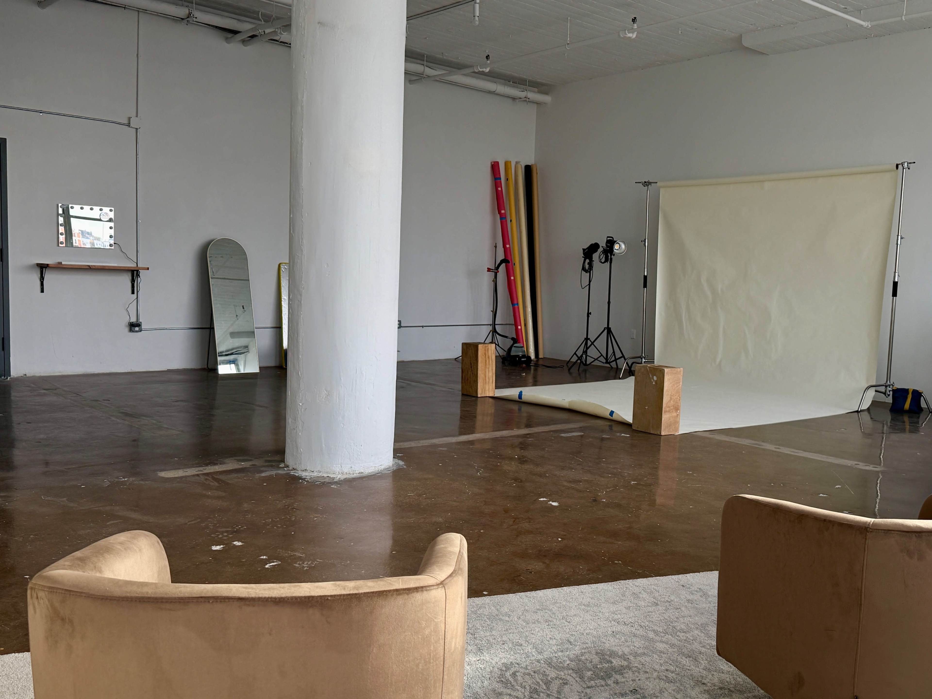 The image shows a spacious, empty studio with a large white backdrop and professional lighting setup, accompanied by colorful surfboards leaning against the wall.