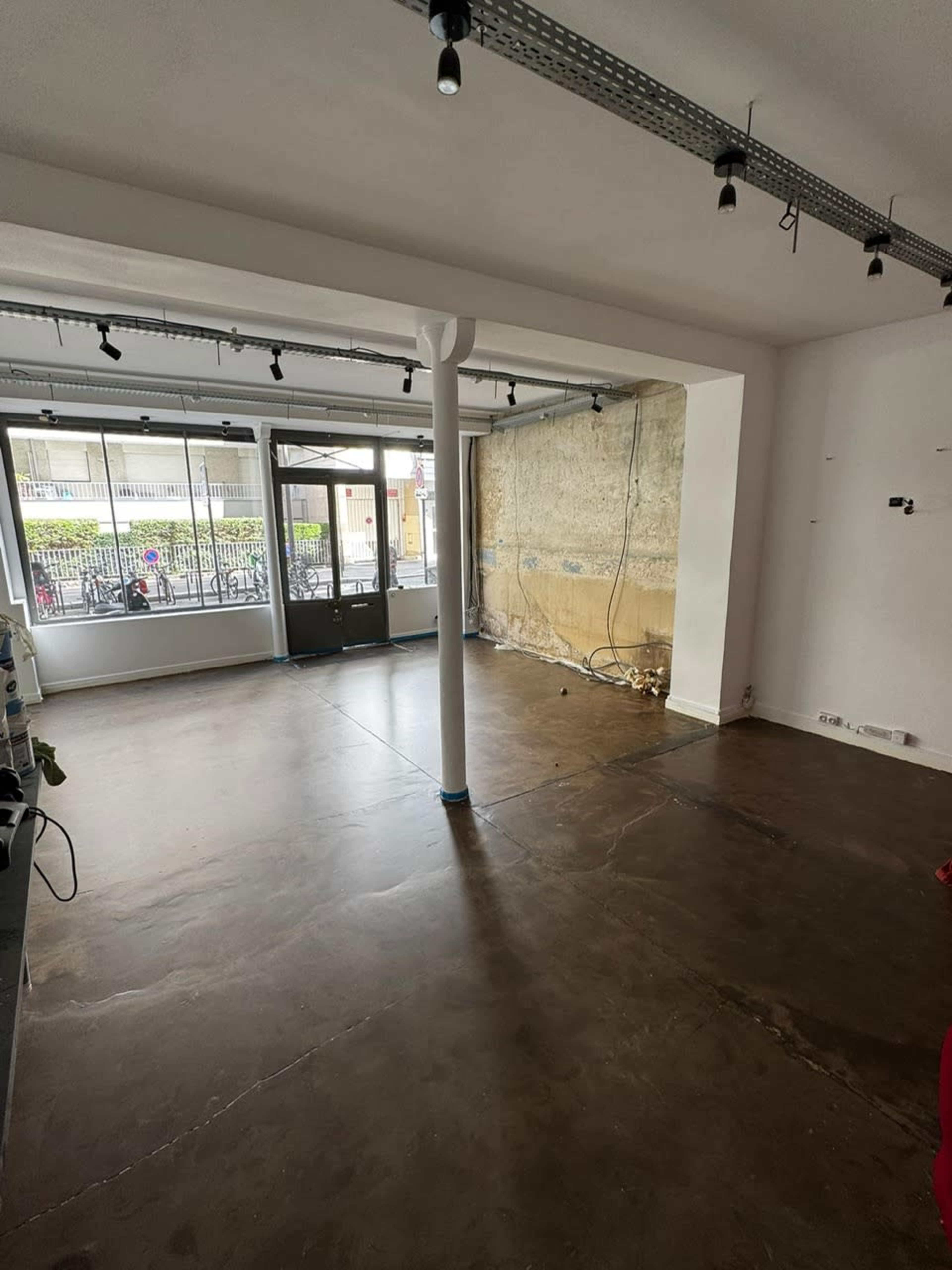 The image shows an empty retail space with a polished concrete floor, bare walls, and large windows allowing natural light to fill the room.