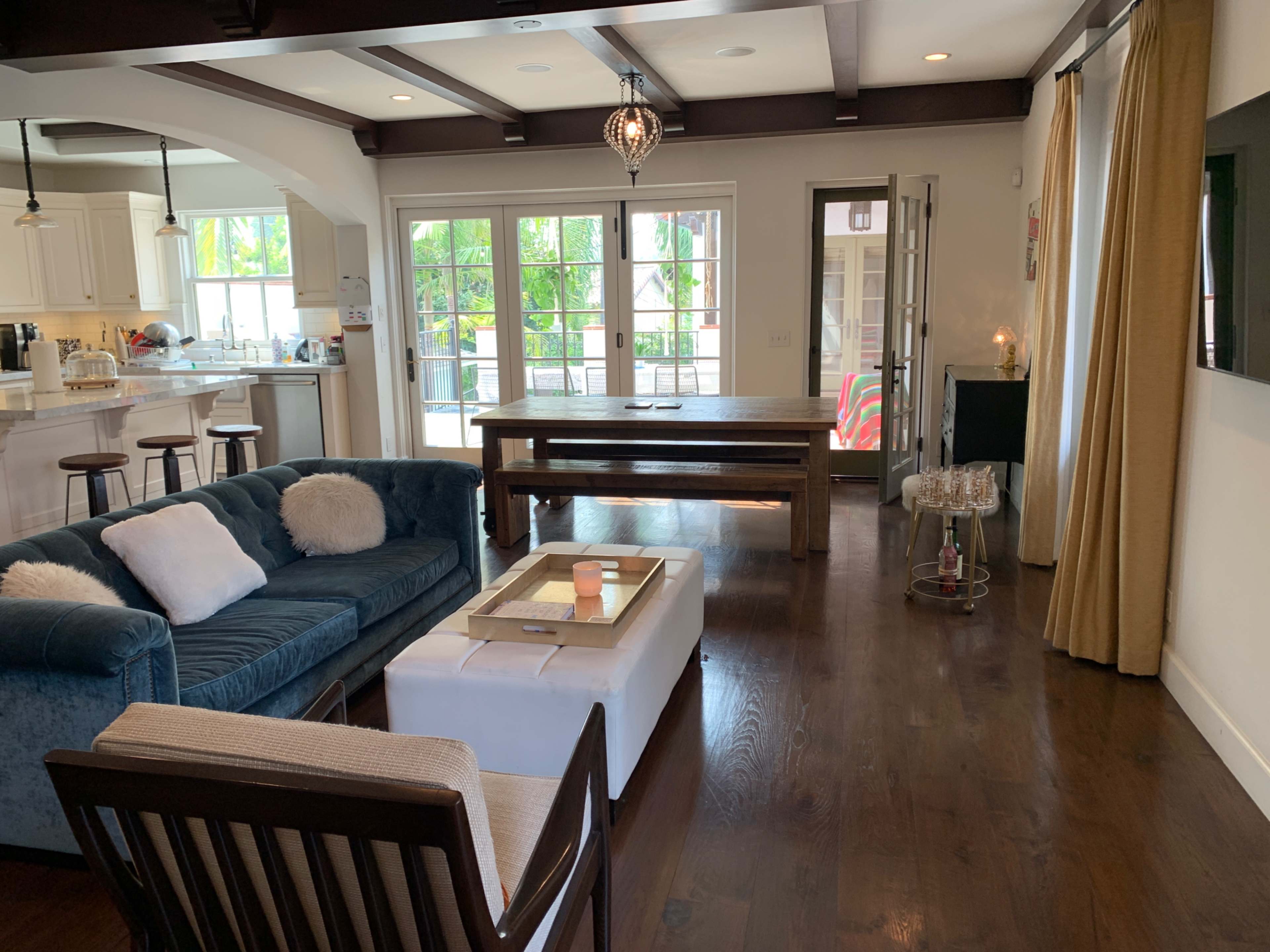 The living area features a blue couch, a white coffee table, and a dining table, with large windows allowing natural light to flood the space.