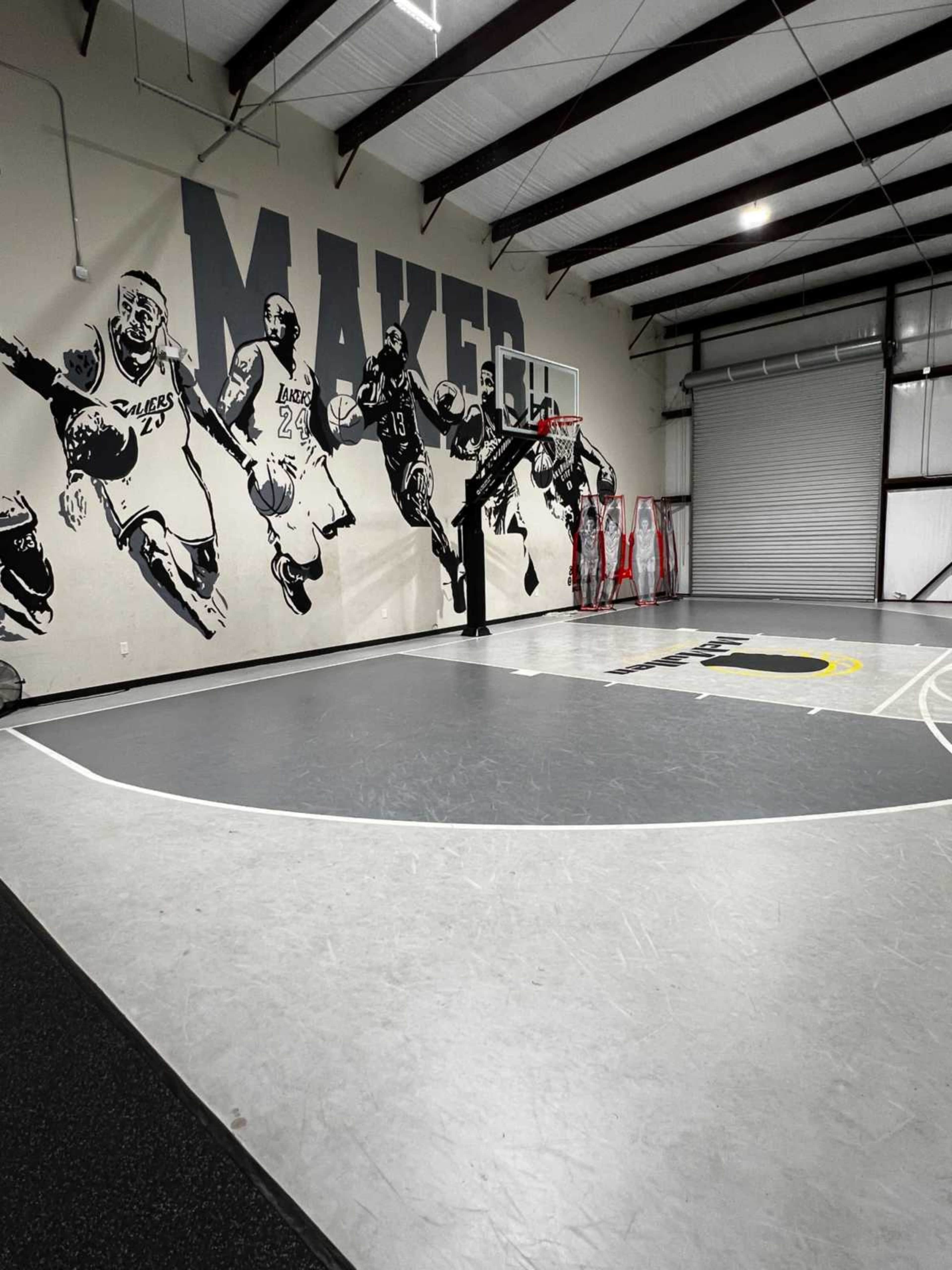 The image shows a basketball court indoors with a large mural of players on the wall and a basketball hoop in the foreground.