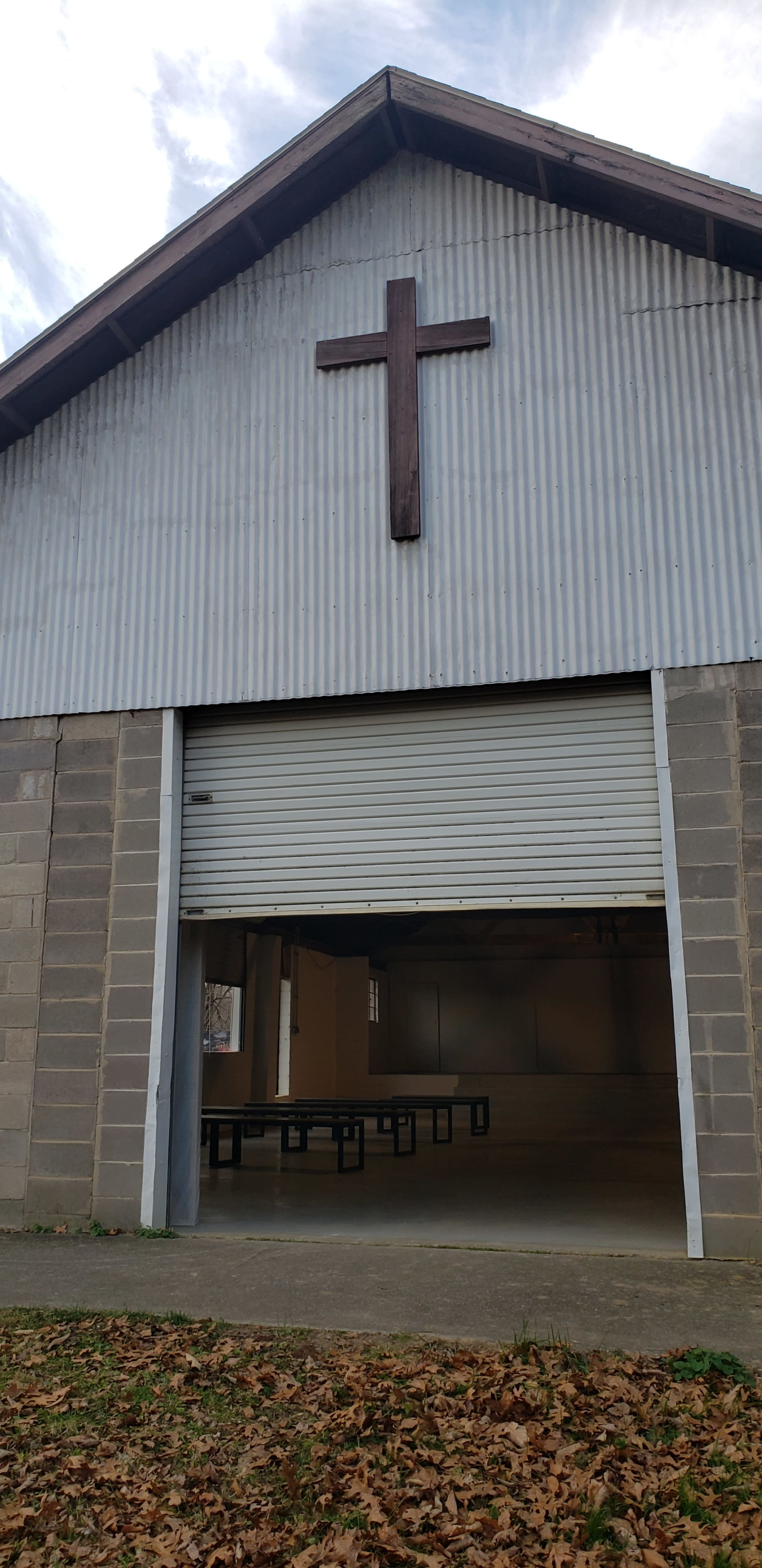 The exterior of a metal building with a large wooden cross above a closed garage-style door.