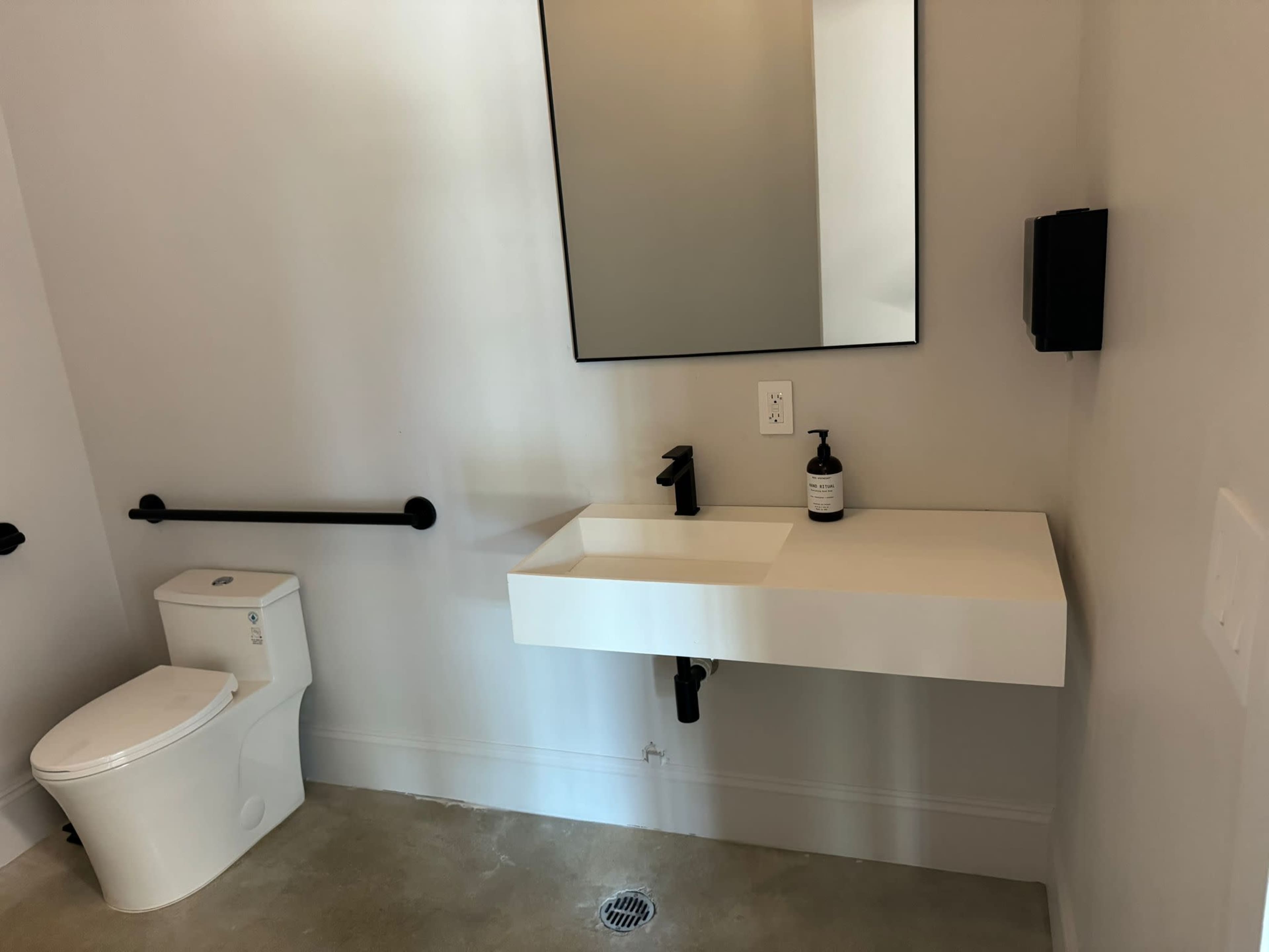 A minimalist bathroom with a wall-mounted sink, a toilet, and a large mirror on the wall.