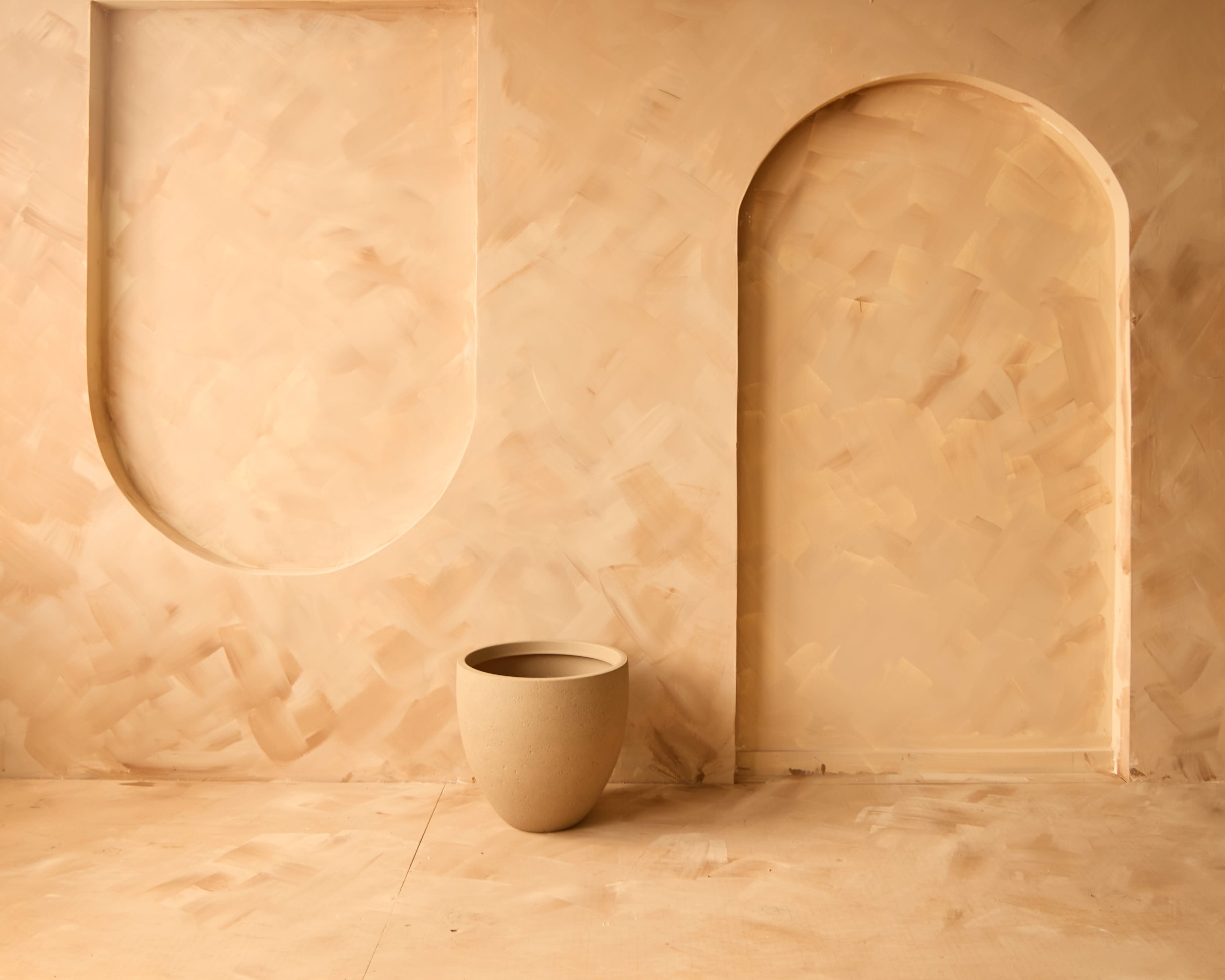 A minimalist interior space featuring a curved arch and a cylindrical pot against a textured, light-toned wall.