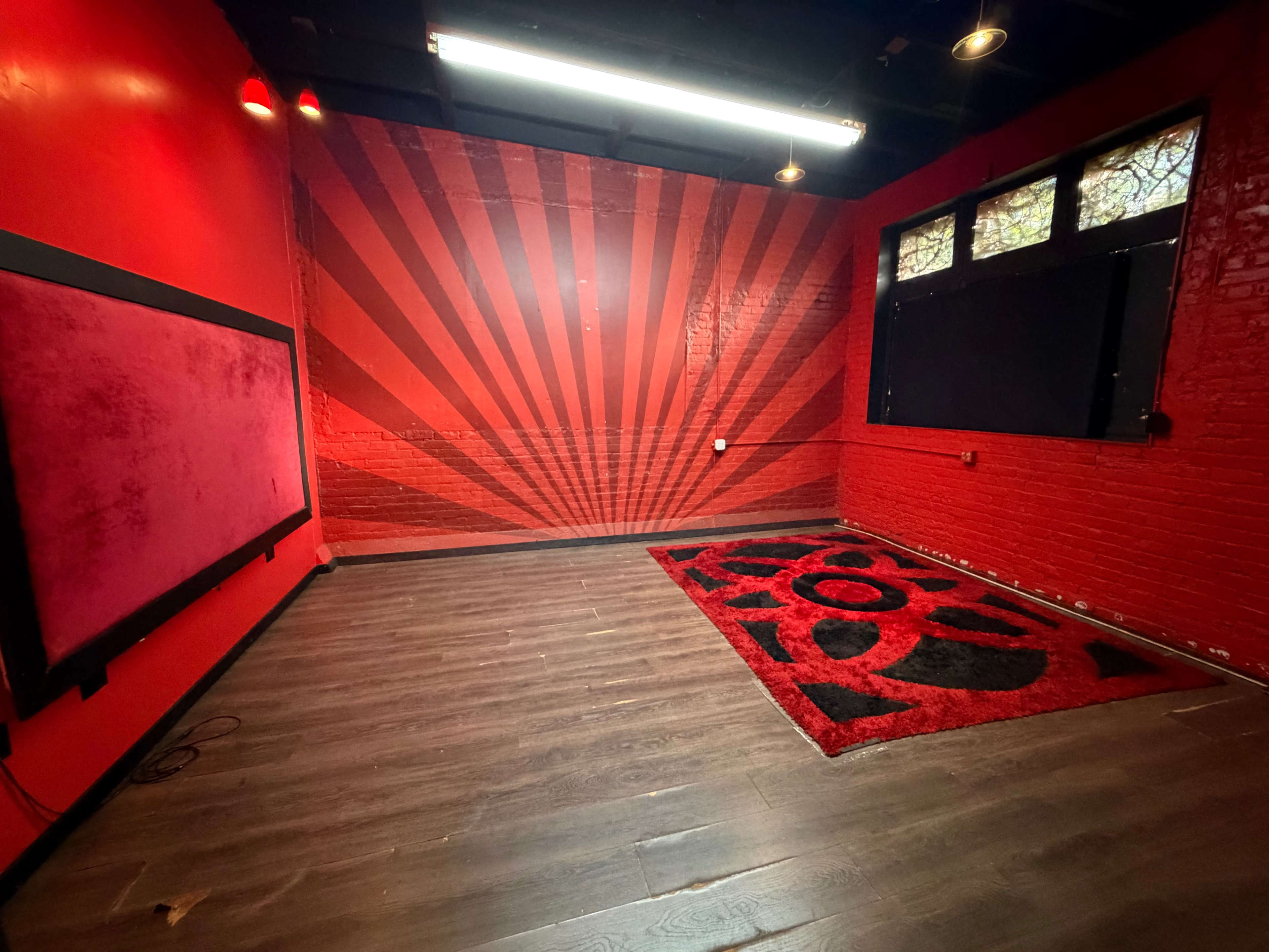 The image shows a room with red walls featuring a large graphic pattern, wooden flooring, and a black and red patterned rug.