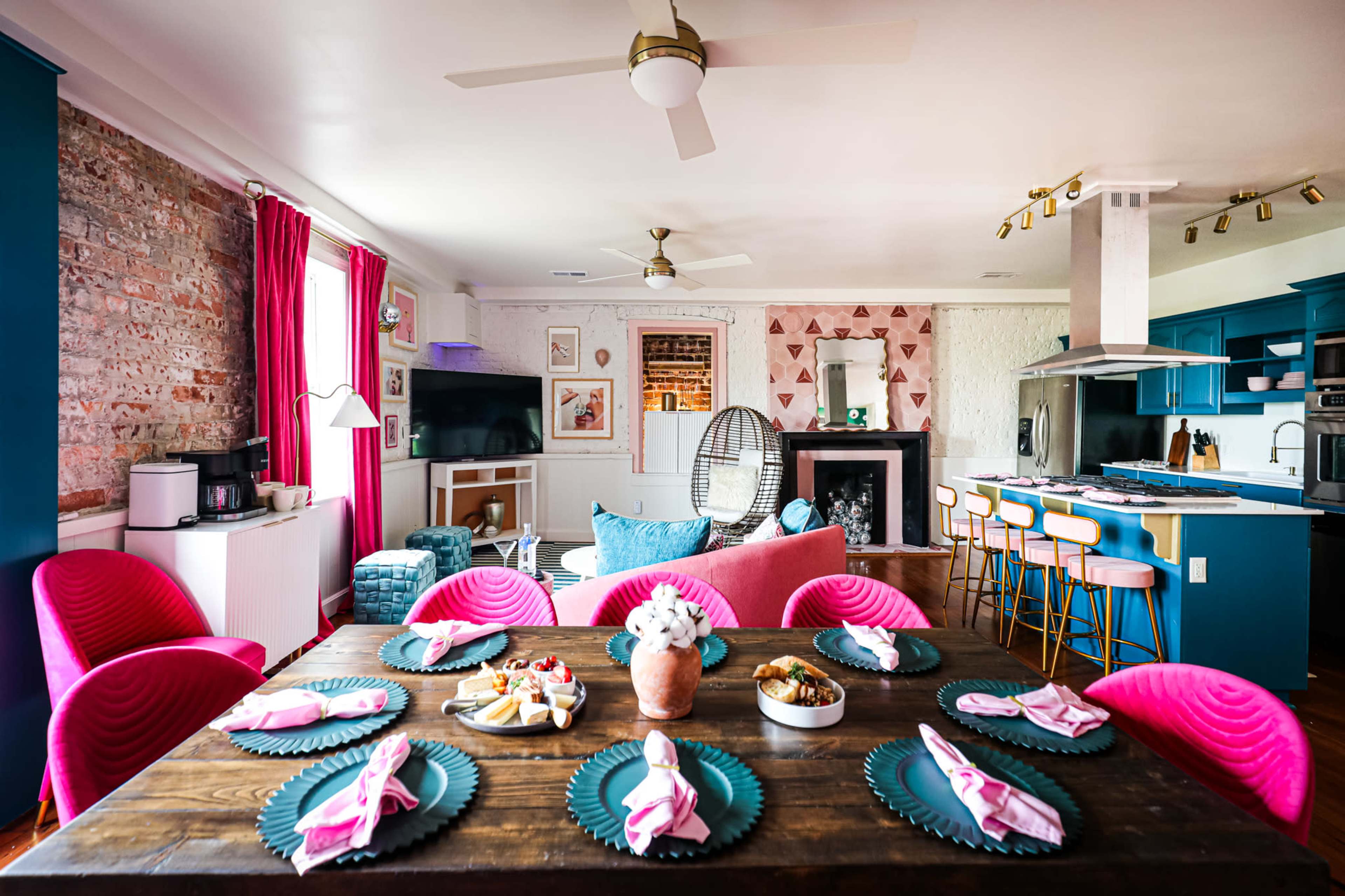 A vibrant living space with a dining table set for a meal, pink chairs, a fireplace, and a modern kitchen area in the background.