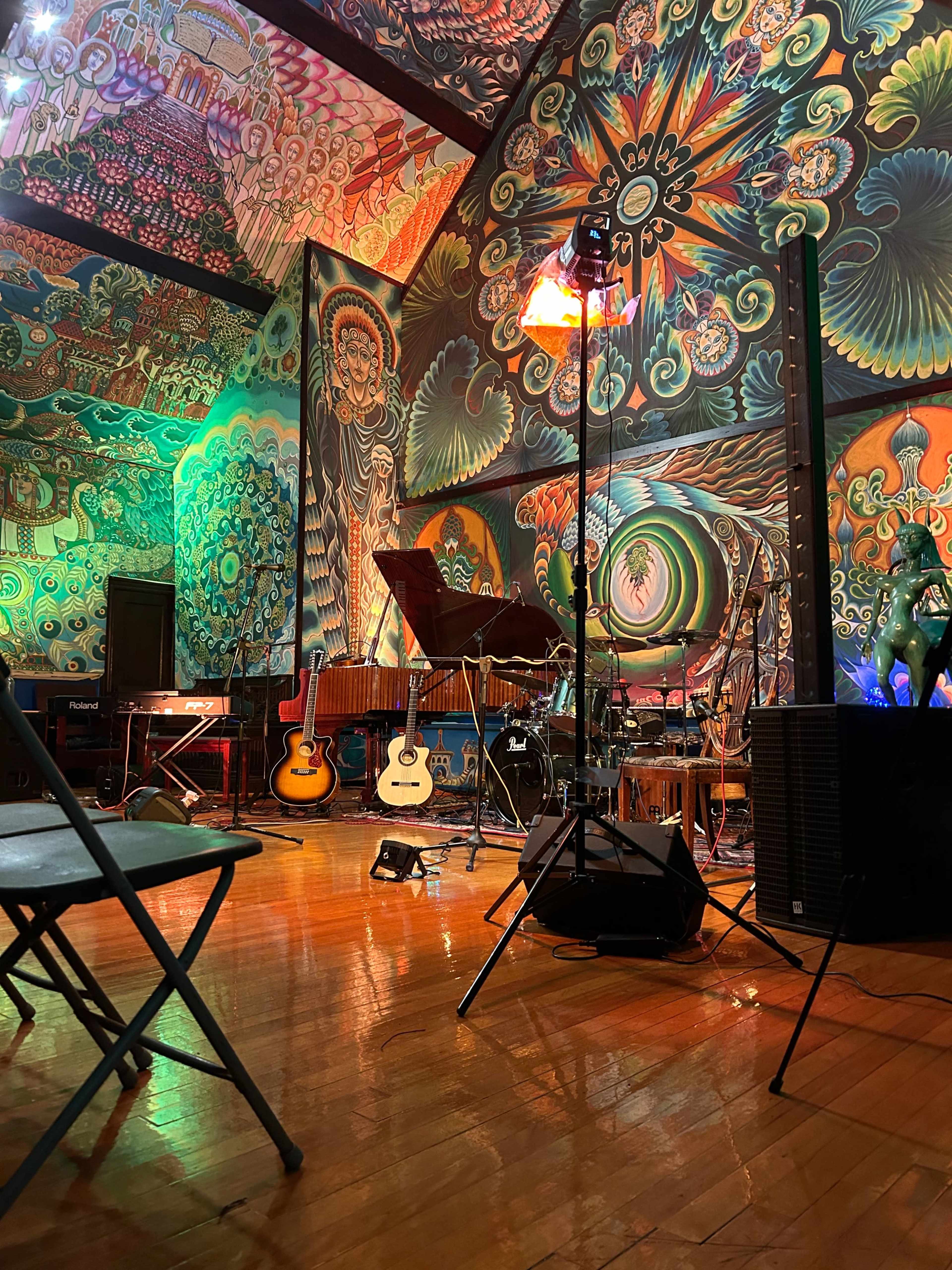 A vibrant room with colorful murals on the walls, various musical instruments set up, and empty chairs arranged for a performance.