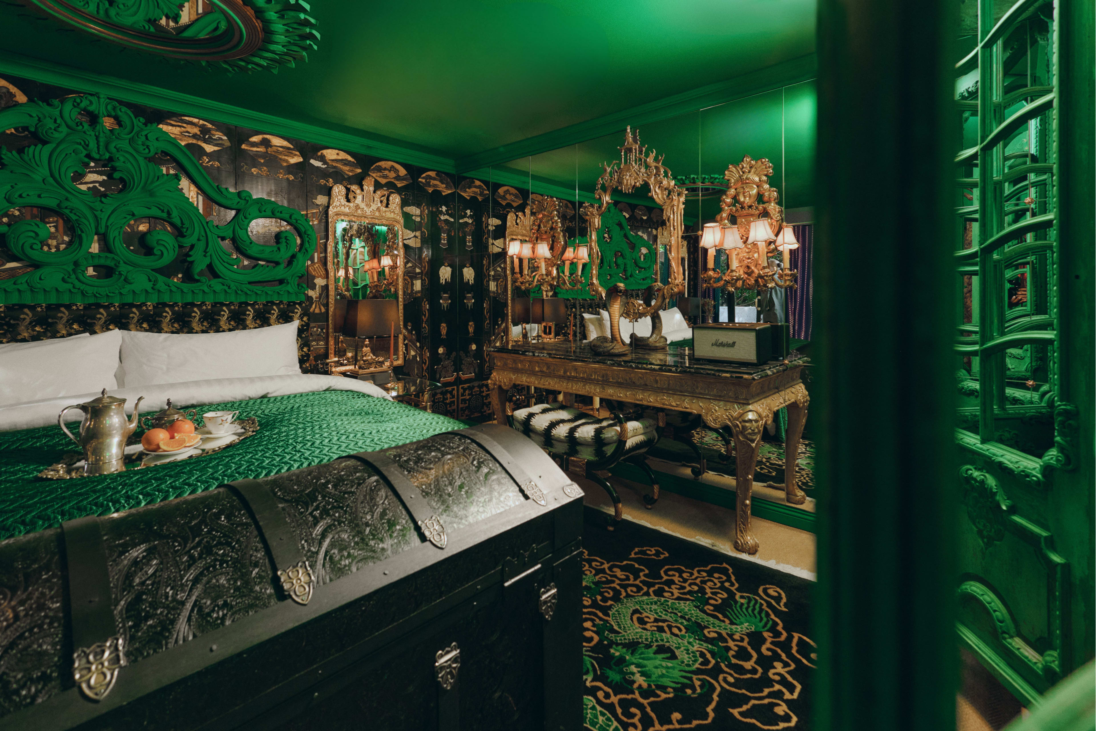The room features rich green decor, a large ornate bed, and antique furnishings alongside modern lighting fixtures.
