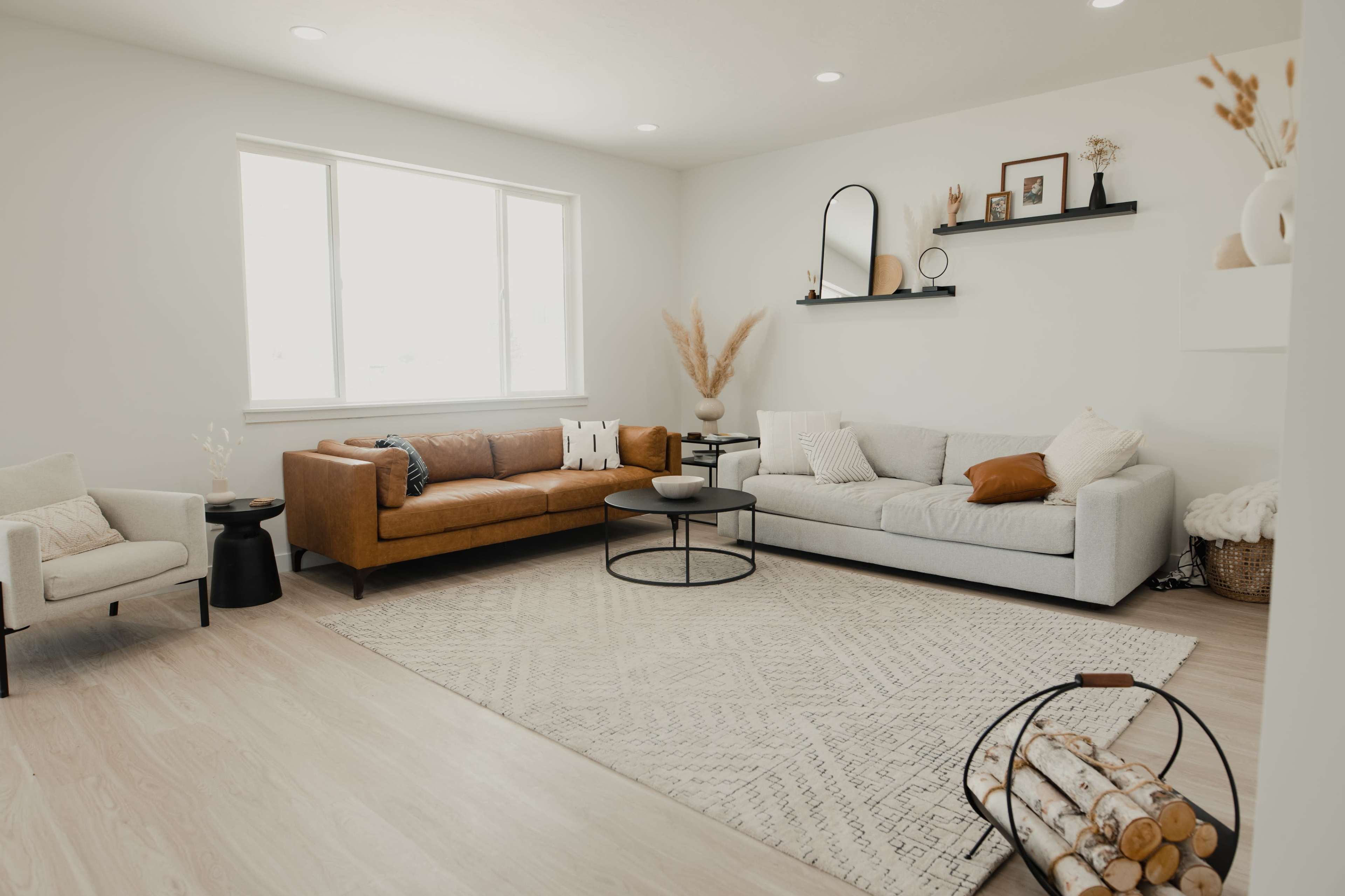 A modern living room with a tan leather sofa, a gray couch, a round coffee table, decorative shelves, and a textured rug.