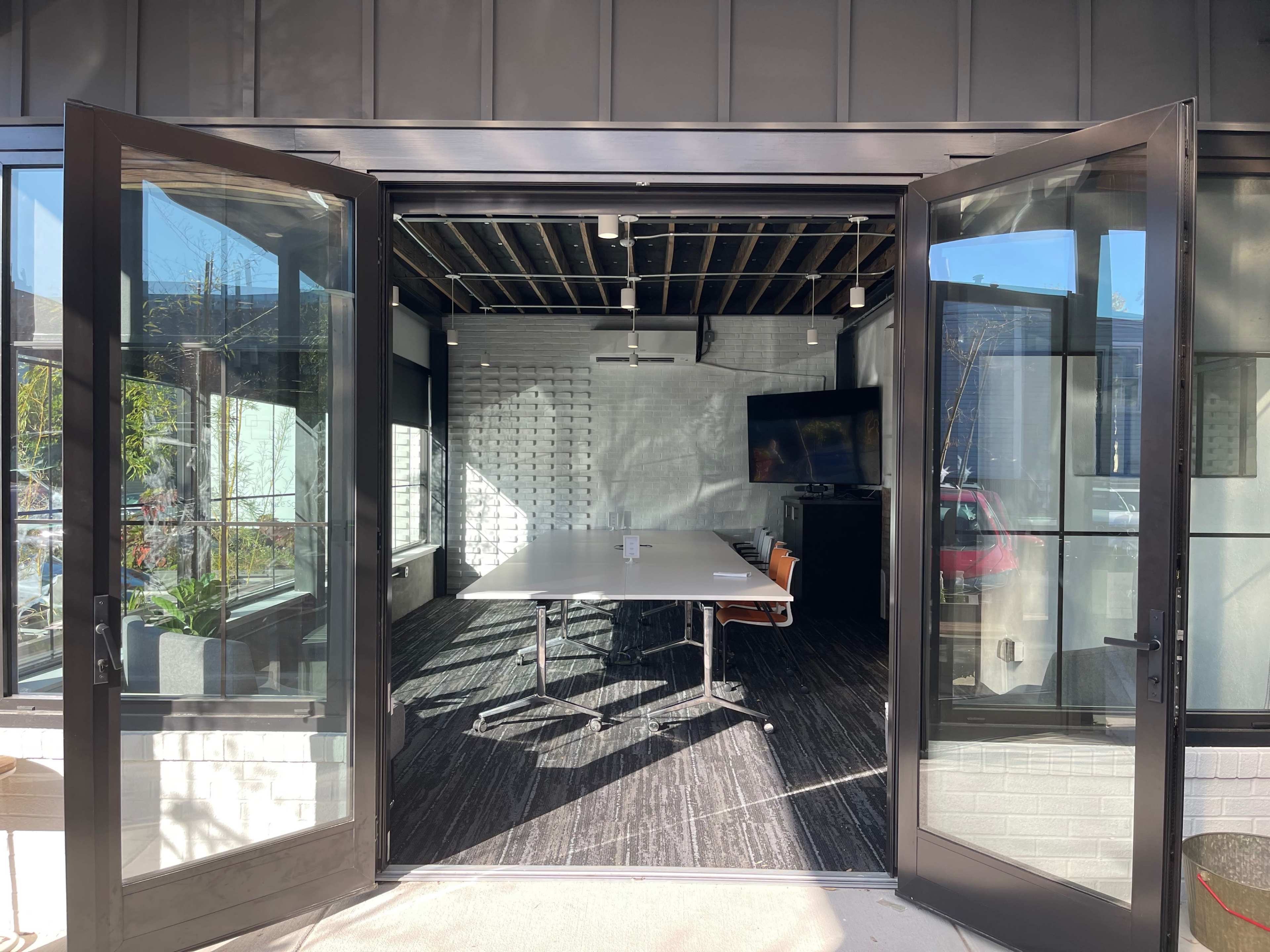 A spacious, modern conference room is visible through open double doors, featuring a large table, a television, and large windows letting in natural light.