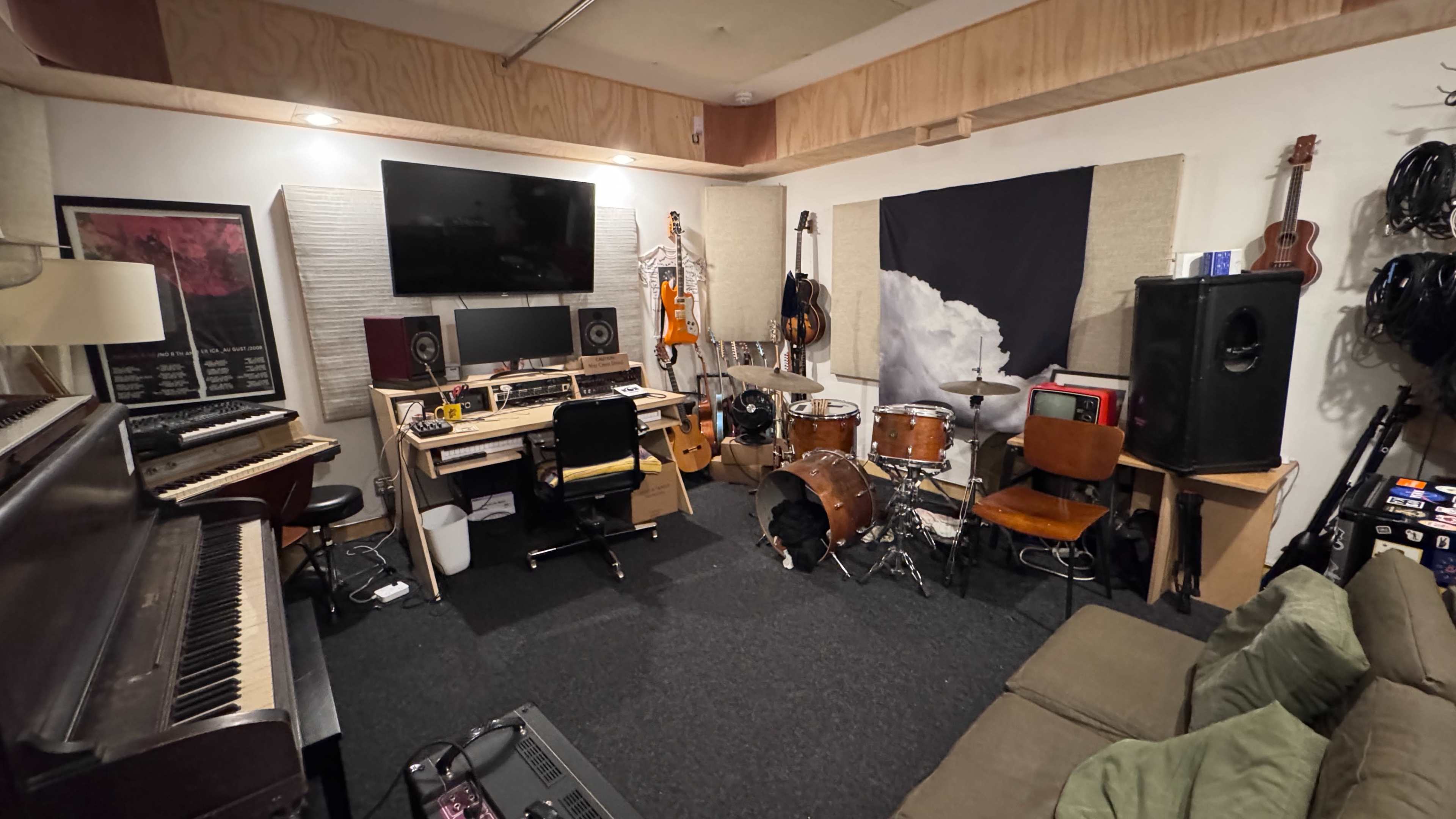 The image shows a music studio with instruments, recording equipment, and seating arrangements on a carpeted floor.