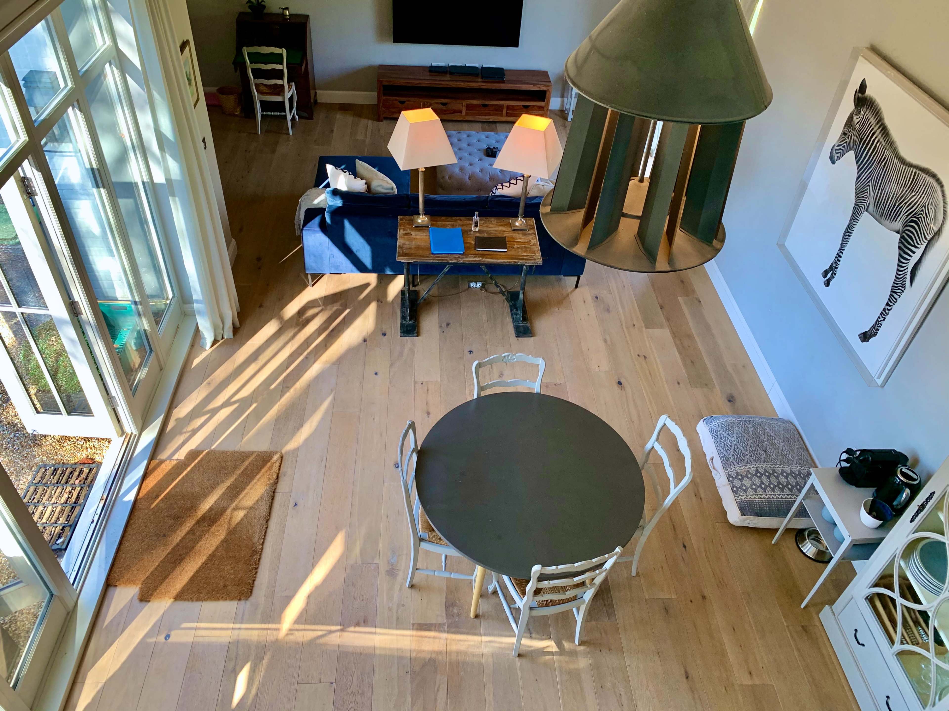 The image shows a bright living space with a blue sofa, a wooden coffee table, a round dining table, and a decorative zebra print on the wall.