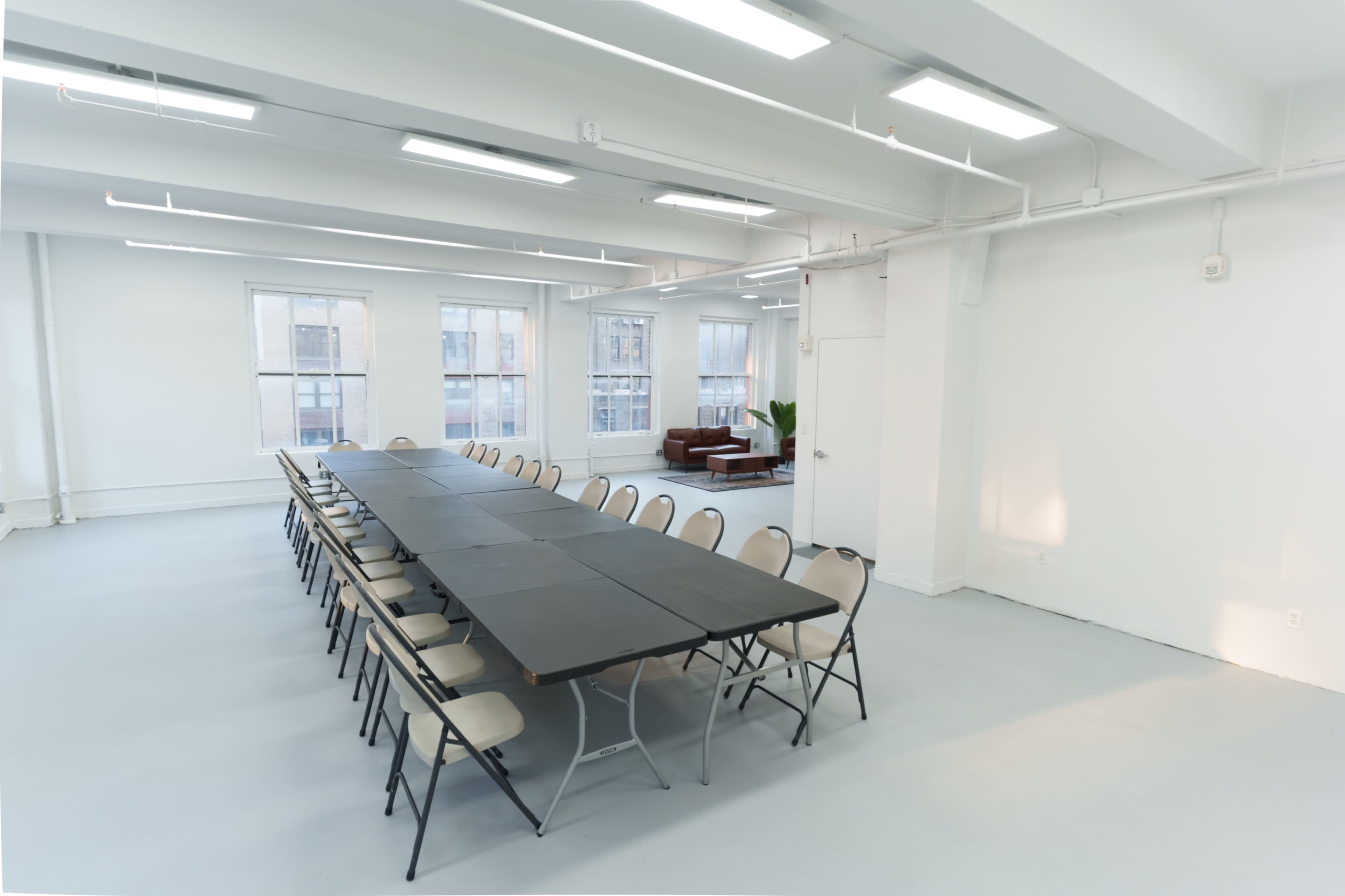 The image shows a spacious, empty meeting room with a long table surrounded by chairs and a seating area in the background.