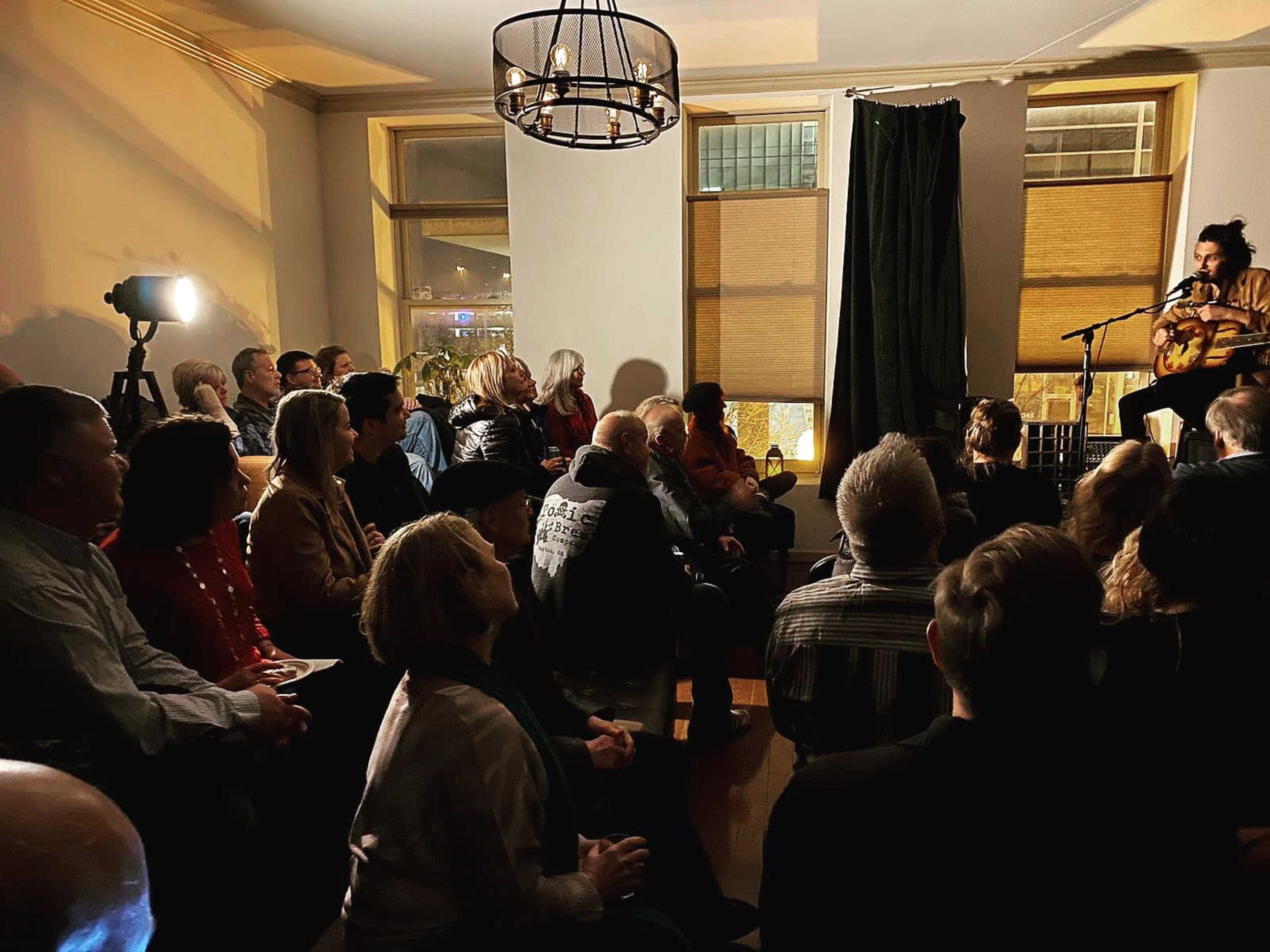 A performer is on stage in front of an audience seated in a softly lit room.