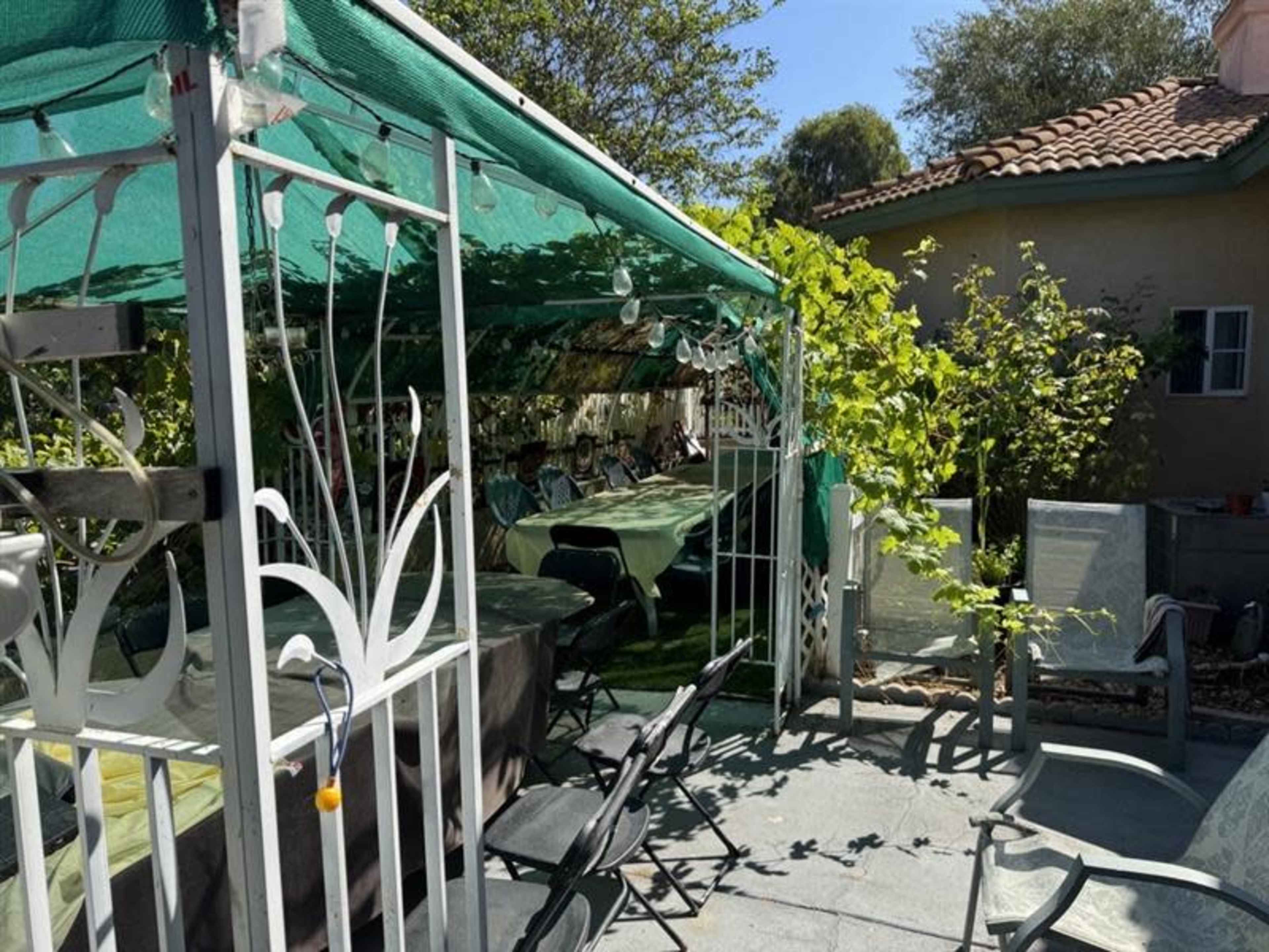 A green canopy covers tables and chairs set up outdoors in a garden area next to a residential building.