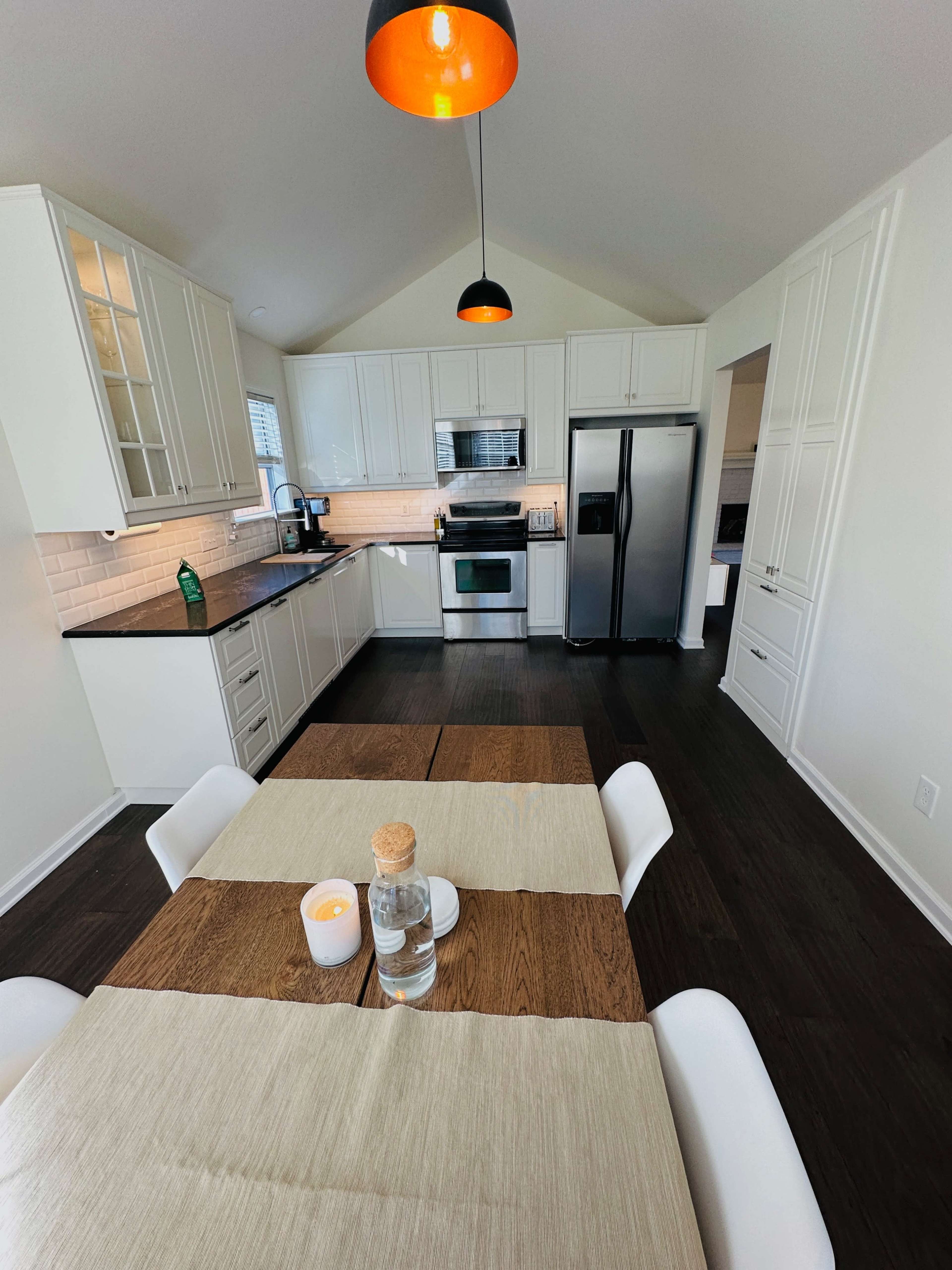 The kitchen features white cabinetry, stainless steel appliances, and a dining table set for two, with a water bottle and candle on it.