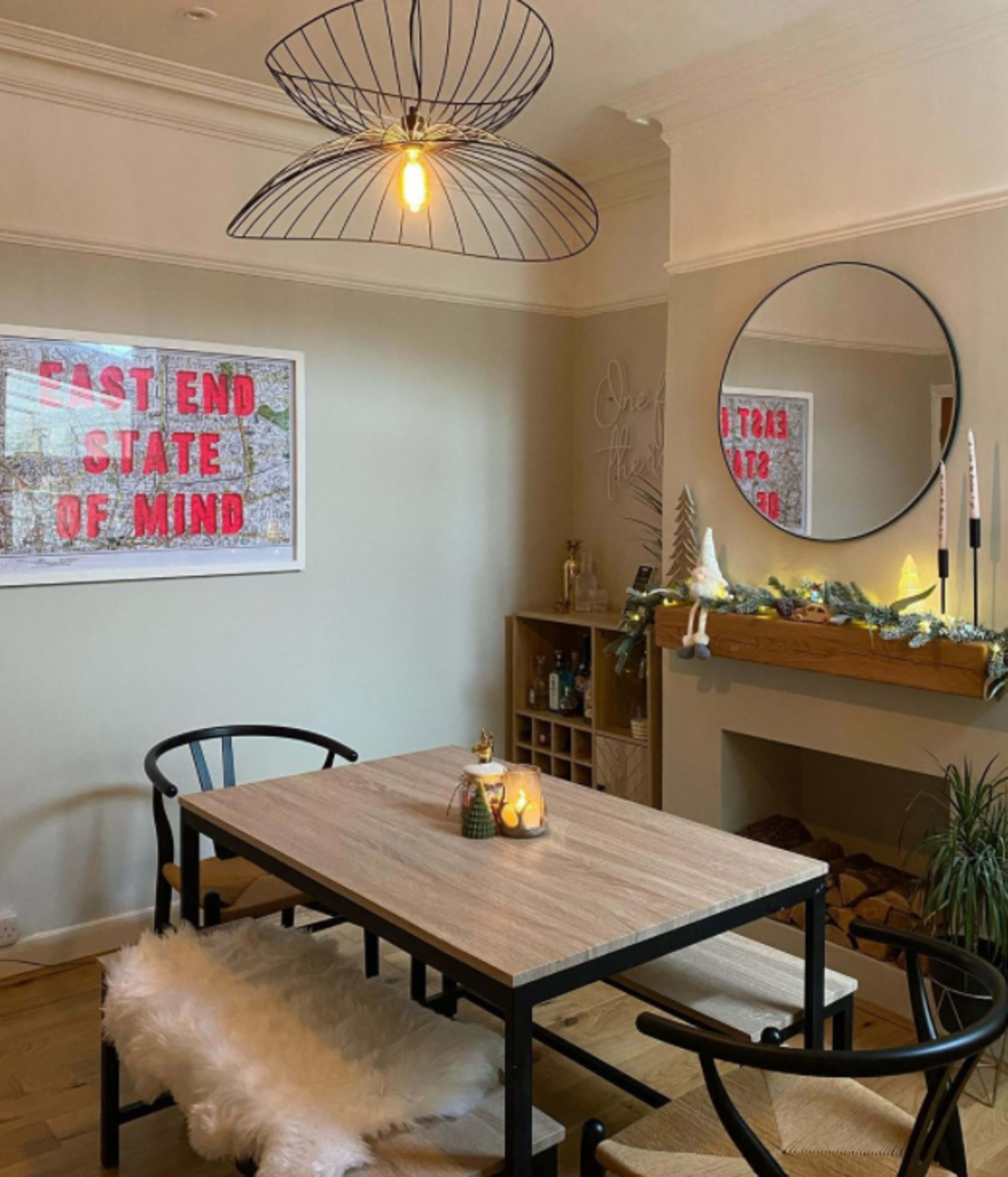 A dining area featuring a wooden table with black chairs, a large circular mirror on the wall, and a decorative string of garland along the mantelpiece.