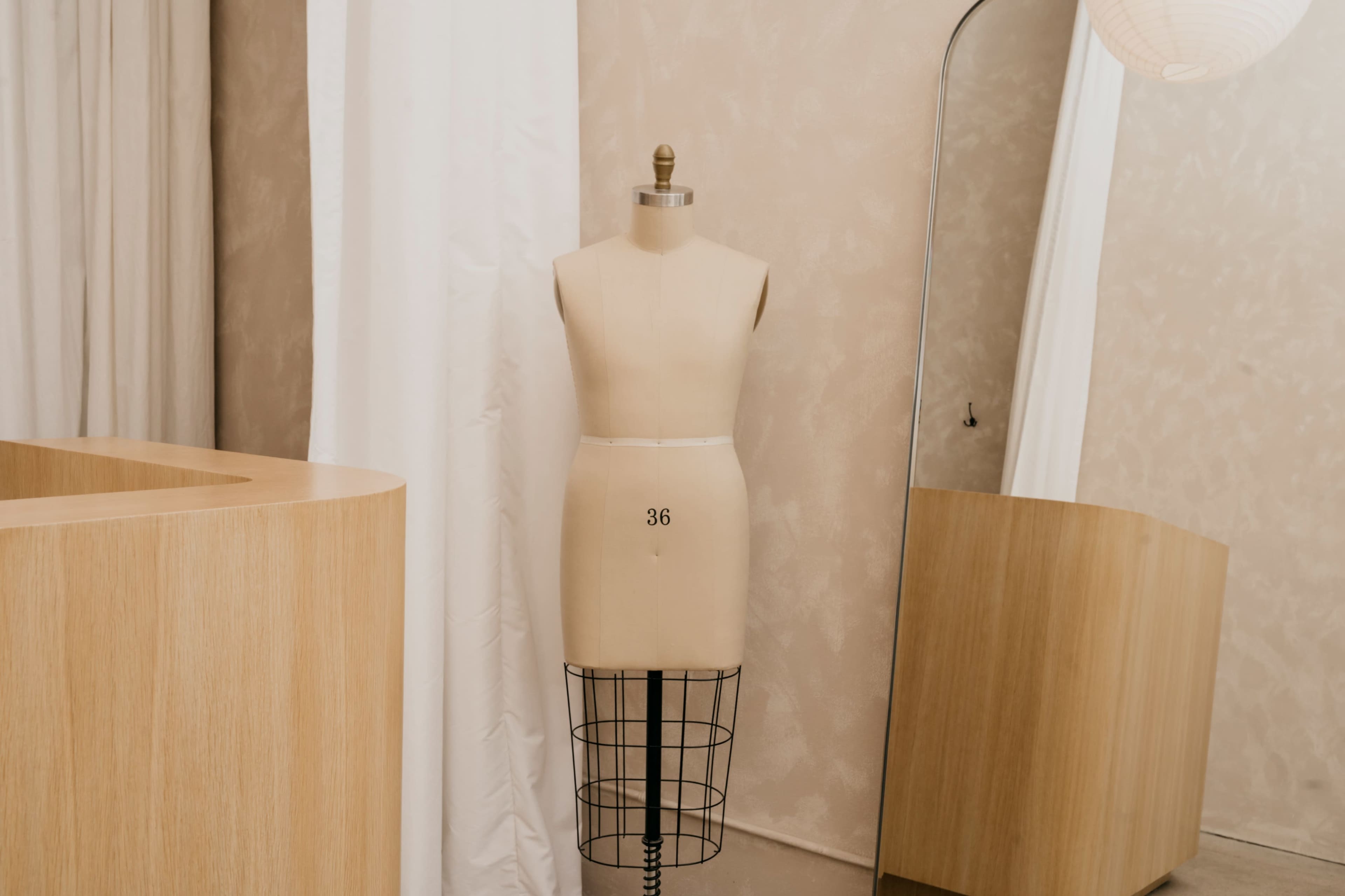 The image shows a dressmakers' mannequin standing in a room with wooden furniture and a mirror.
