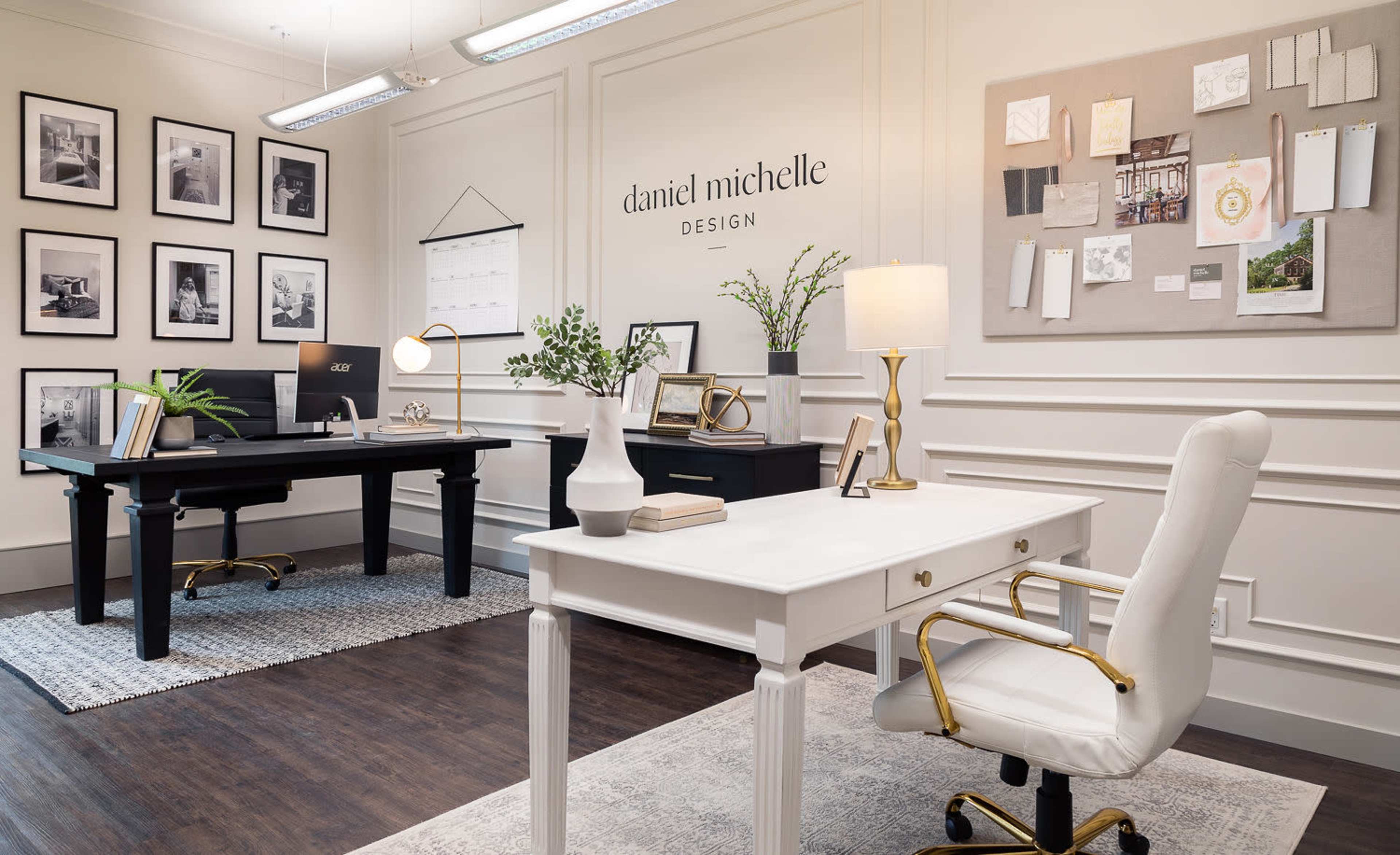 A modern office space with a black desk on the left, a white desk with a gold-accented chair on the right, and a gallery wall of framed photos in a well-lit room.