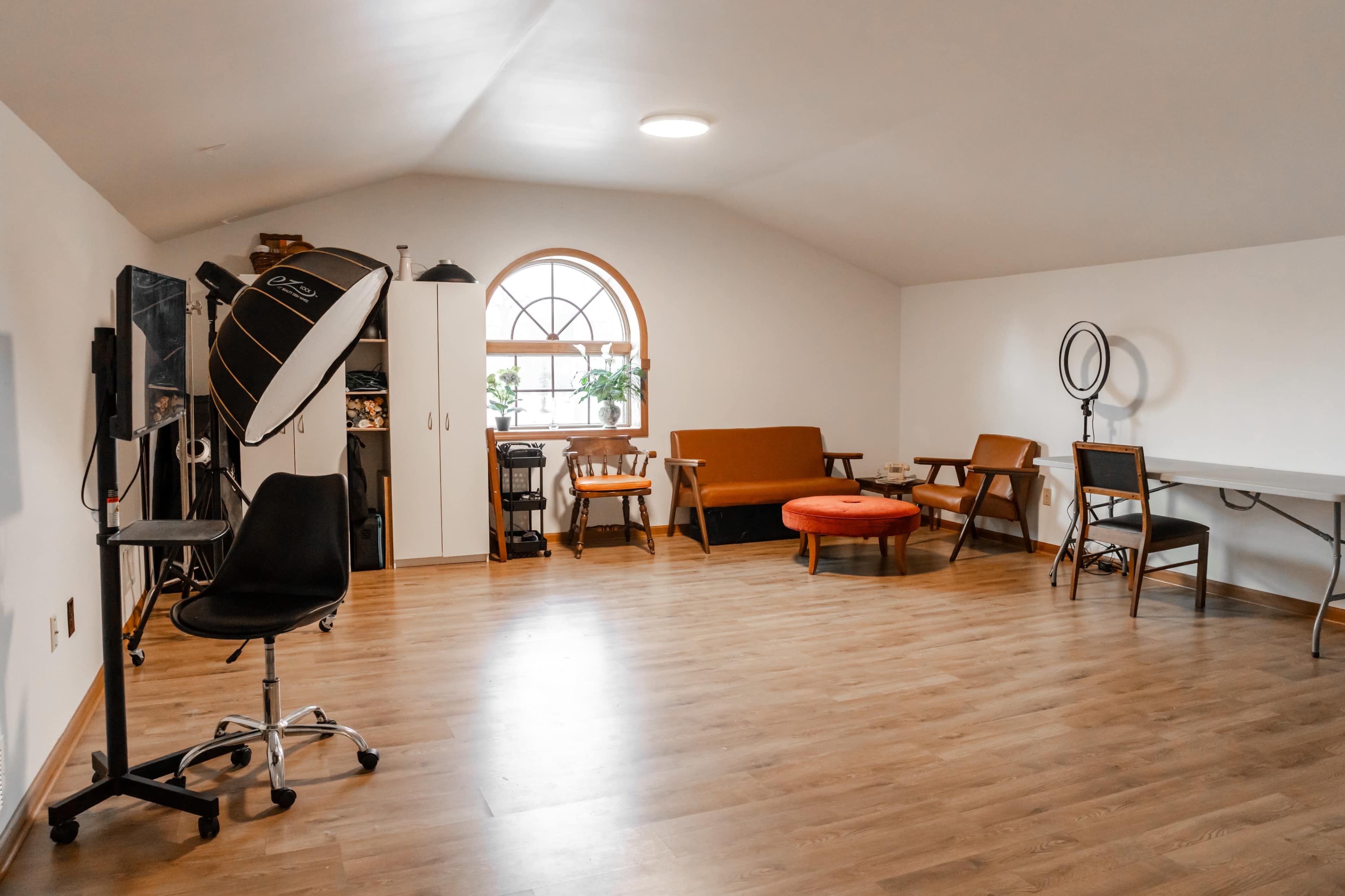 A spacious, well-lit room featuring a mix of furniture, including a sofa, chairs, a table, and a backdrop for photography.