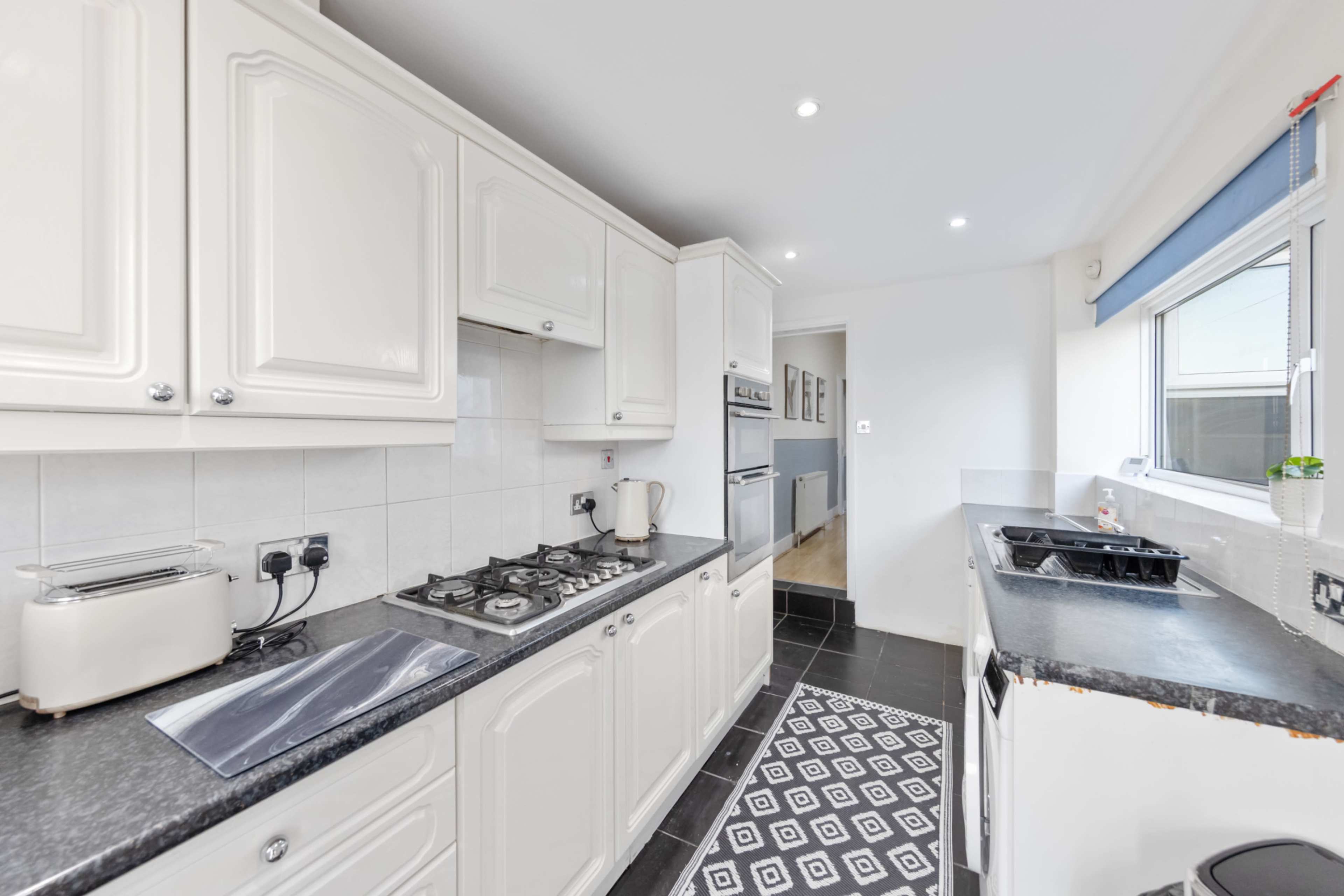 The image shows a modern kitchen featuring white cabinetry, a black countertop, and stainless steel appliances.