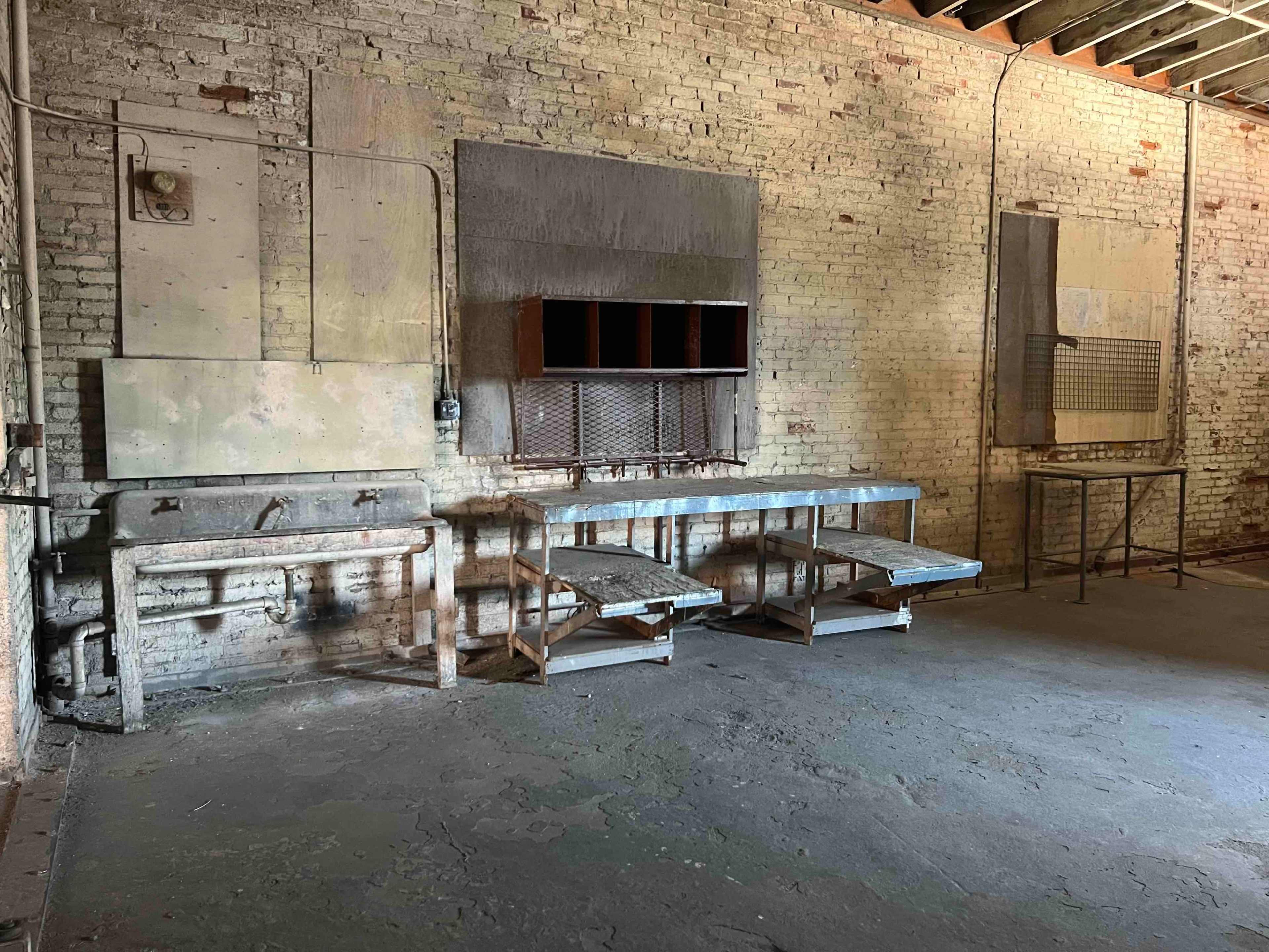 An empty industrial room with a concrete floor, exposed brick walls, and a metal workbench against the wall.