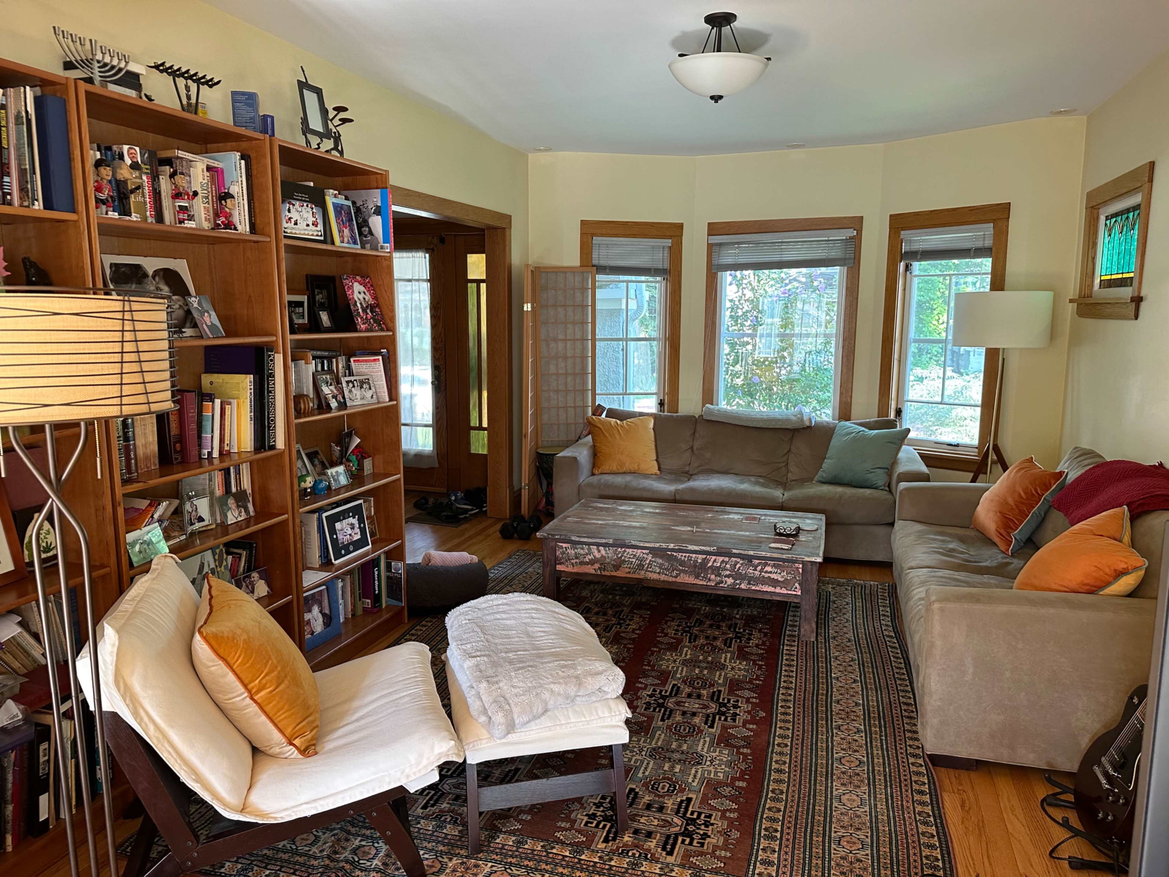 A cozy living room features a light-colored sofa, a wooden coffee table, a patterned rug, and a bookshelf filled with books and decorative items.