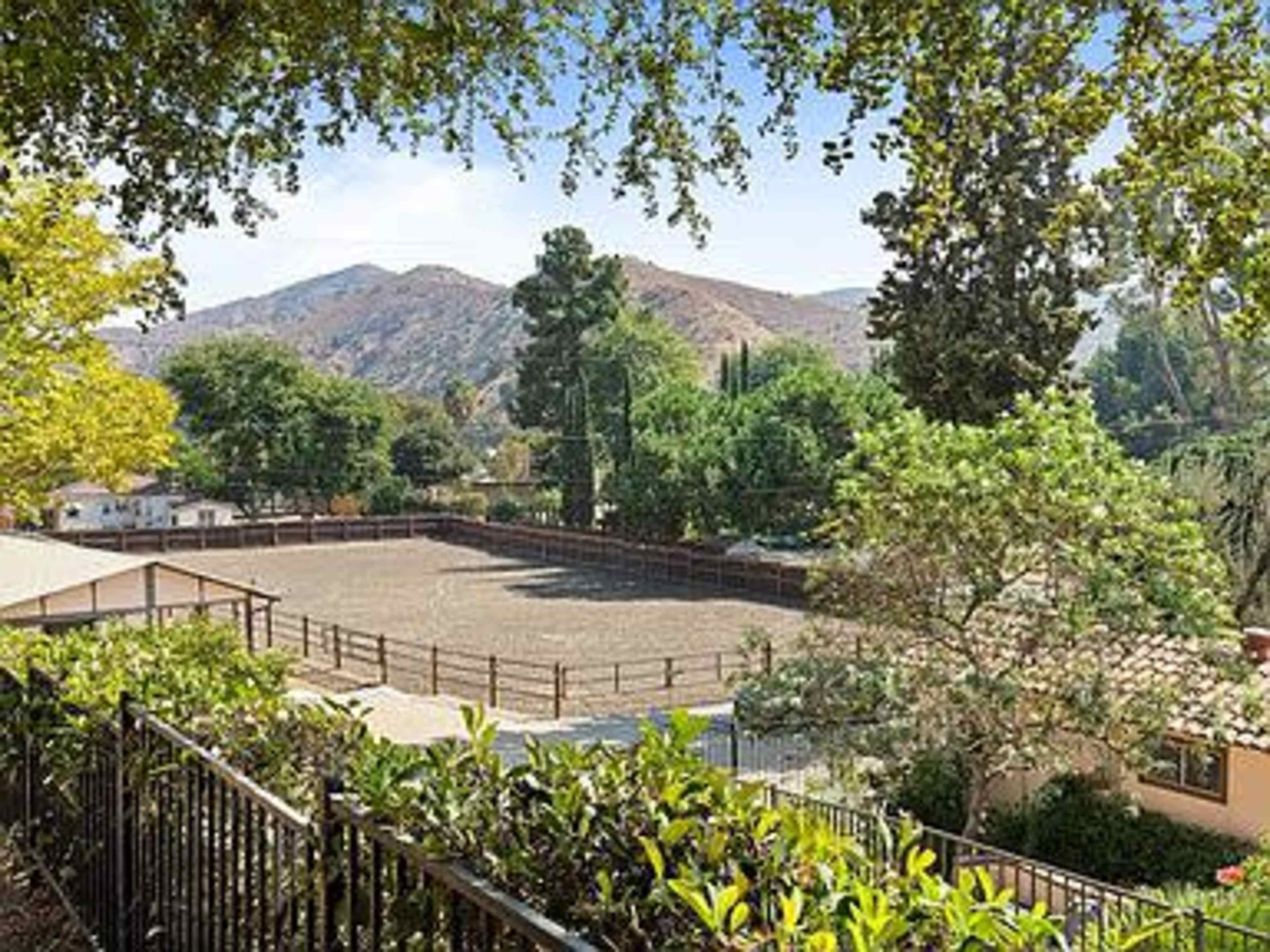 A view of a fenced equestrian arena surrounded by trees and mountains in the background.
