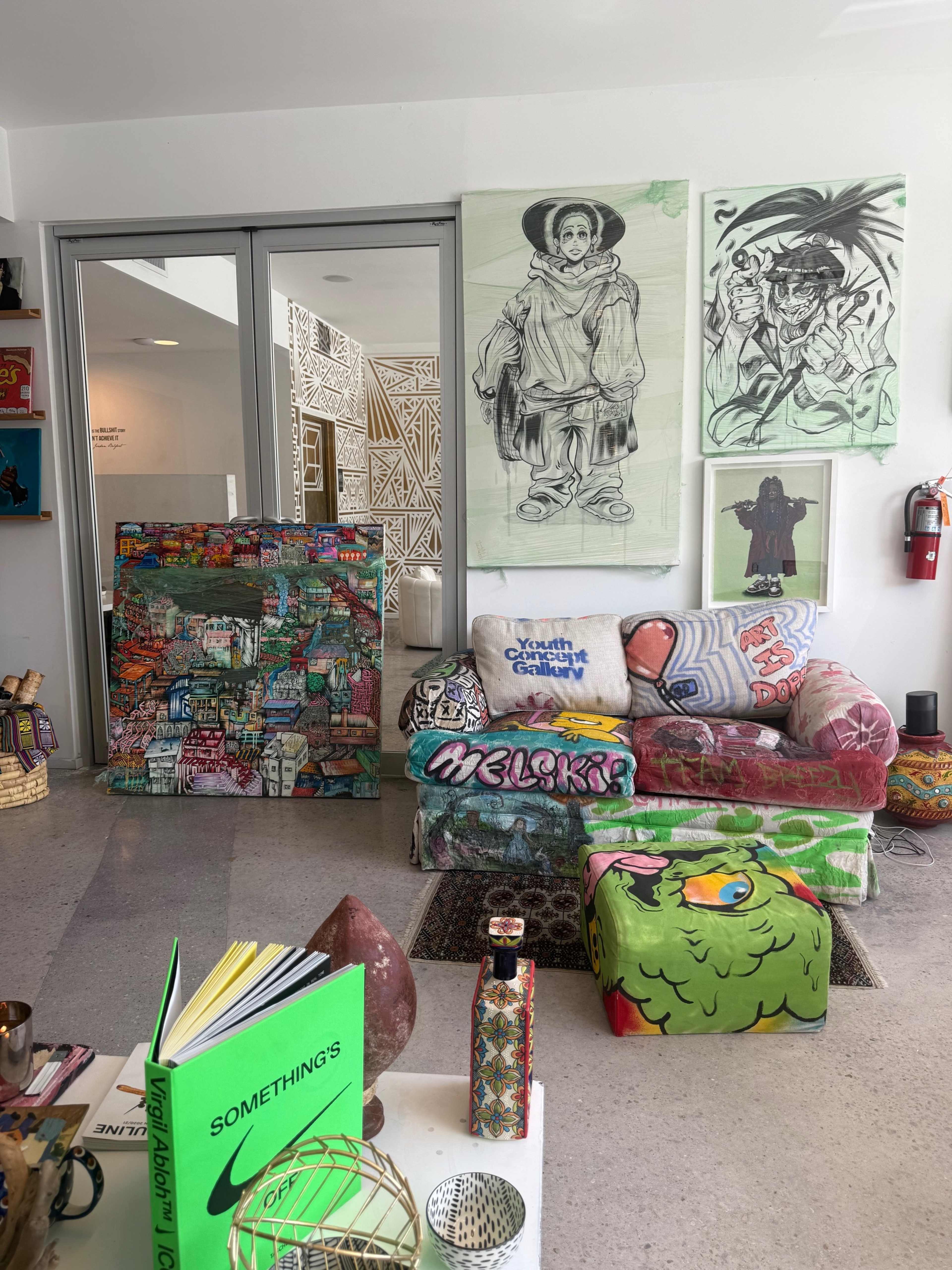 The image shows a colorful living space with a graffiti-covered couch, vibrant decorative stools, and art pieces hanging on the walls.