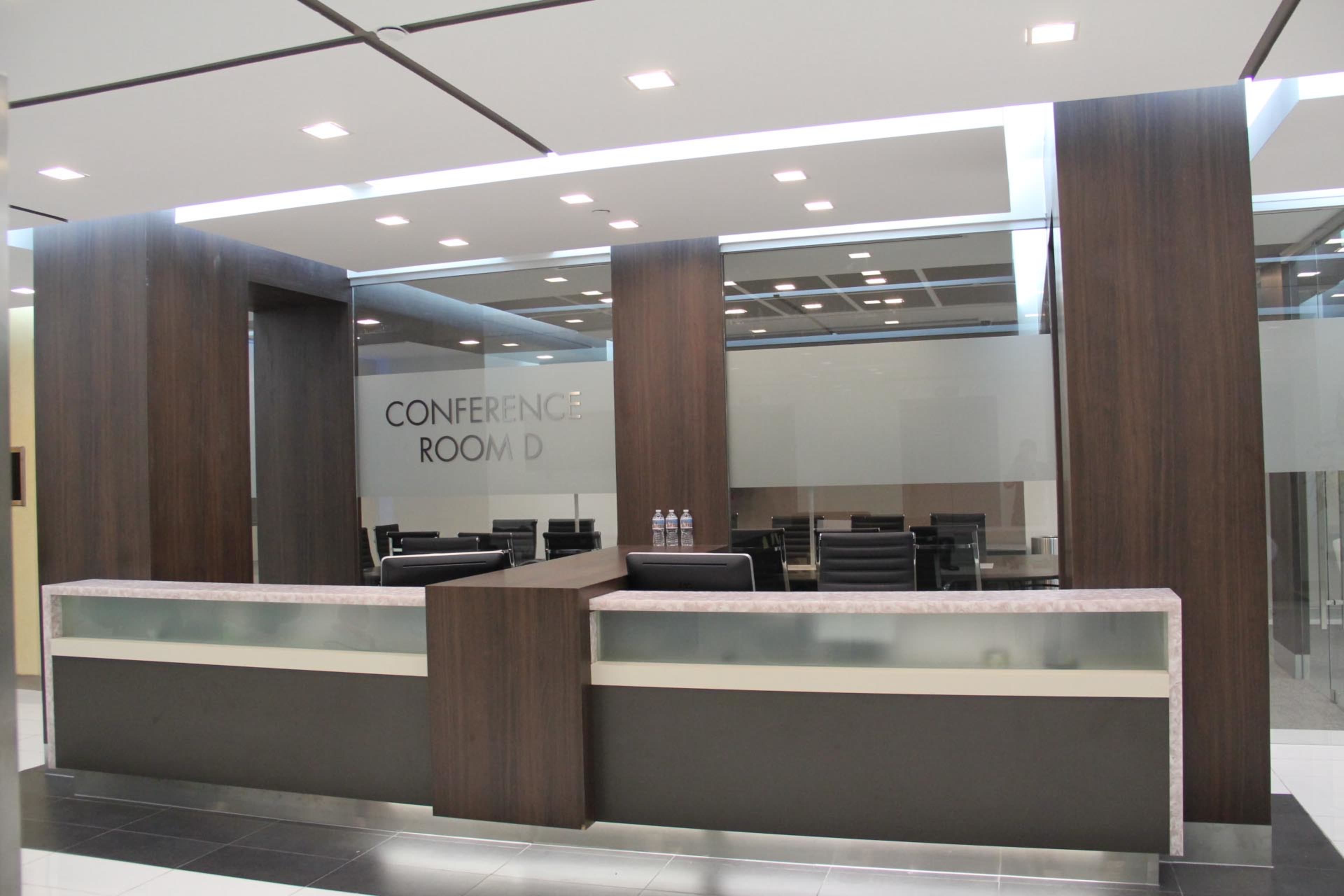 The image shows a modern reception area with a sleek desk and a conference room labeled "Conference Room D" in the background.