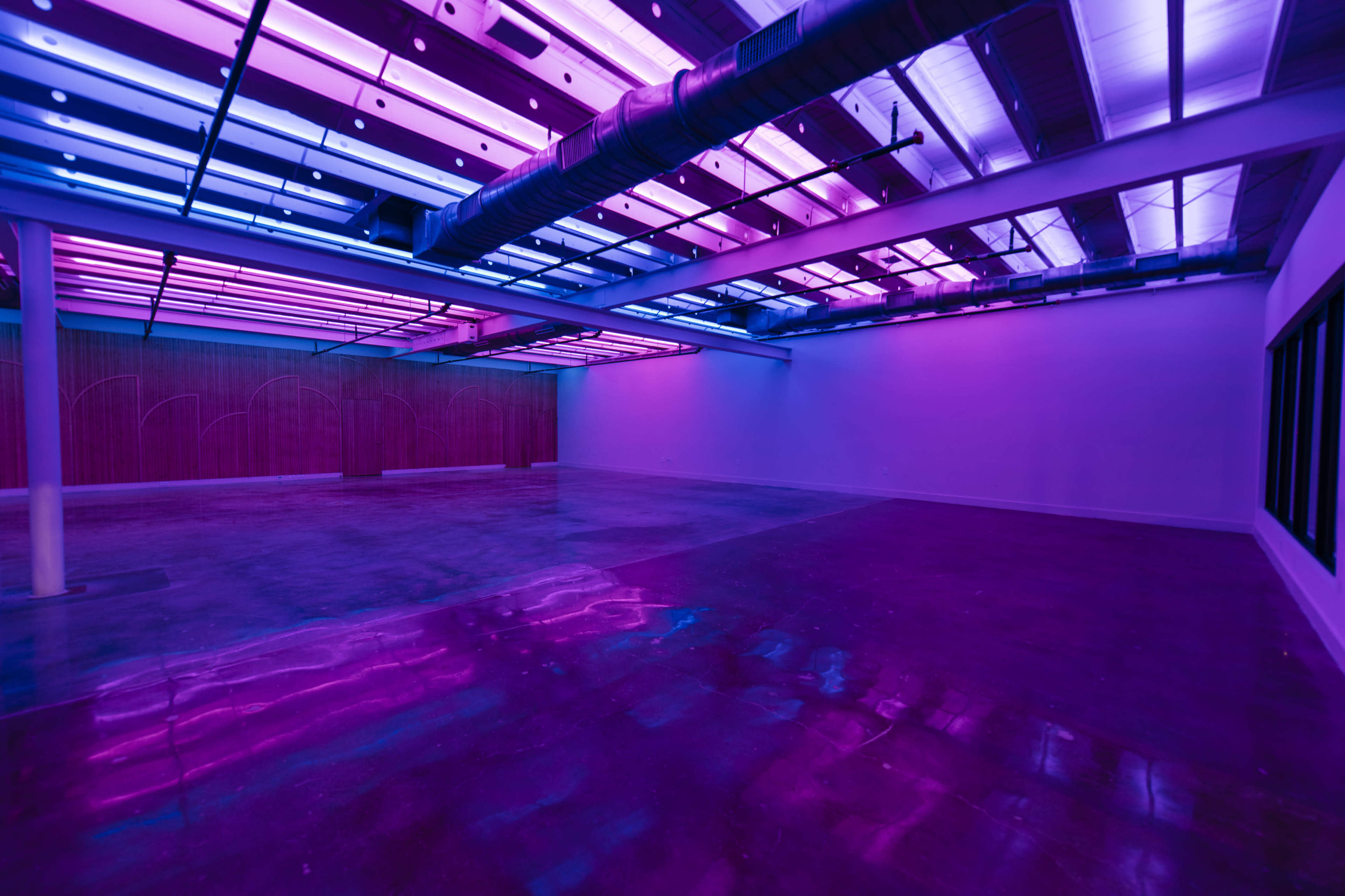 An empty room with glossy concrete floors and vibrant purple and blue LED lighting along the ceiling.