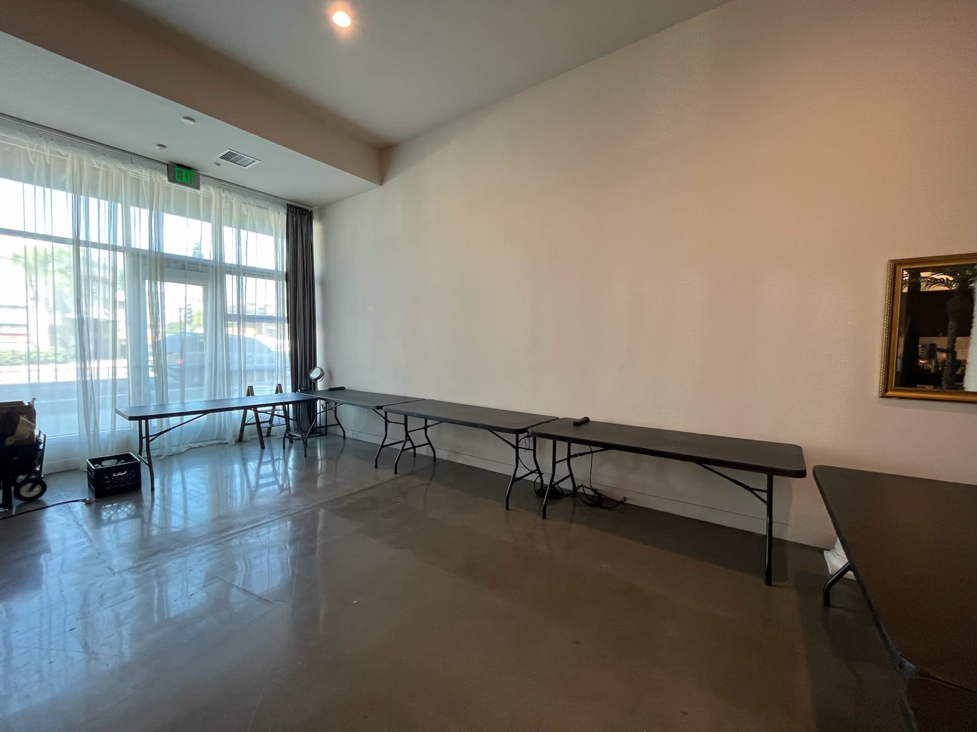 The room features several folding tables arranged against a wall with large windows allowing natural light.