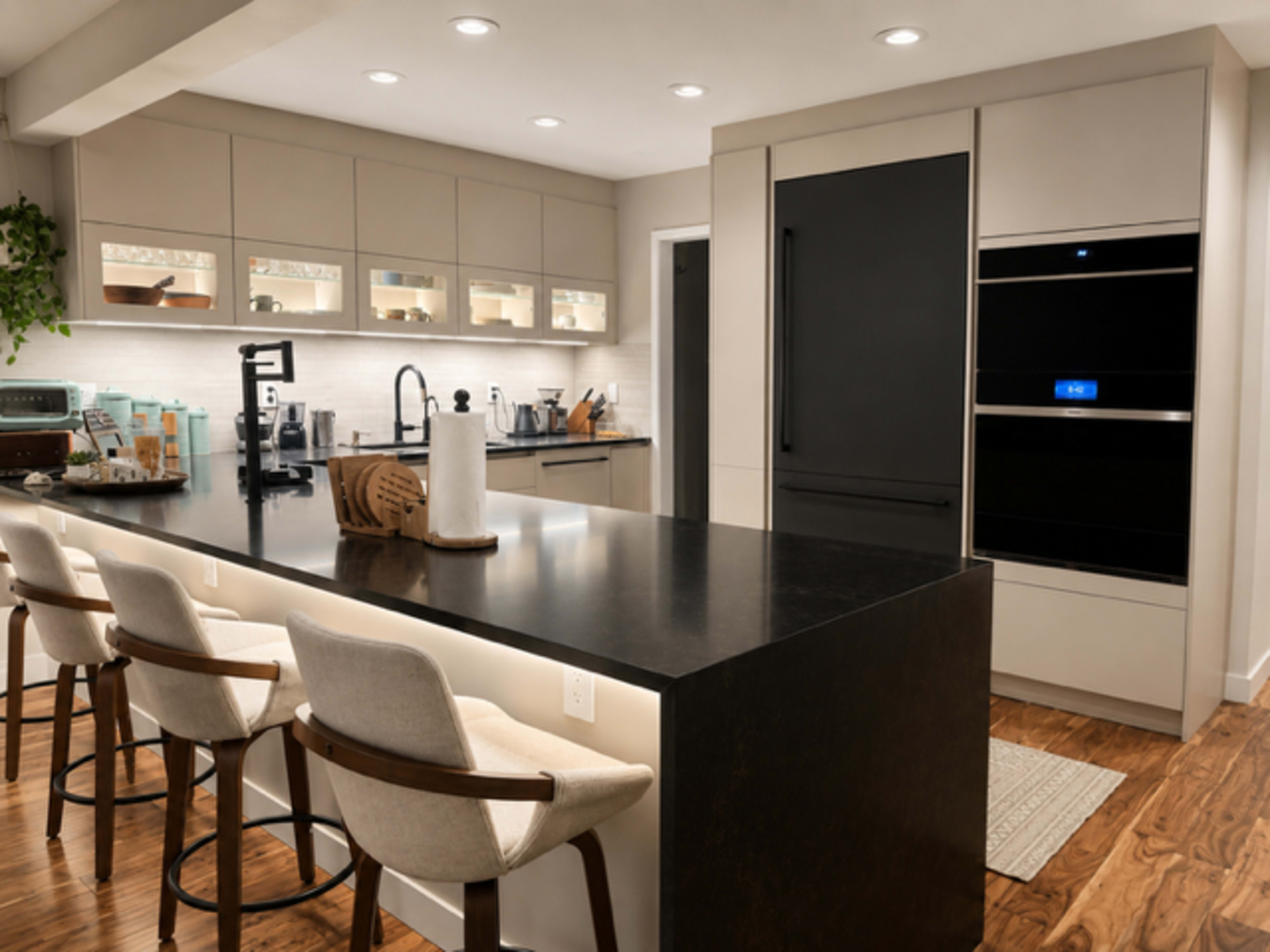 A modern kitchen features a large central island with bar stools, sleek cabinetry, and high-end appliances.