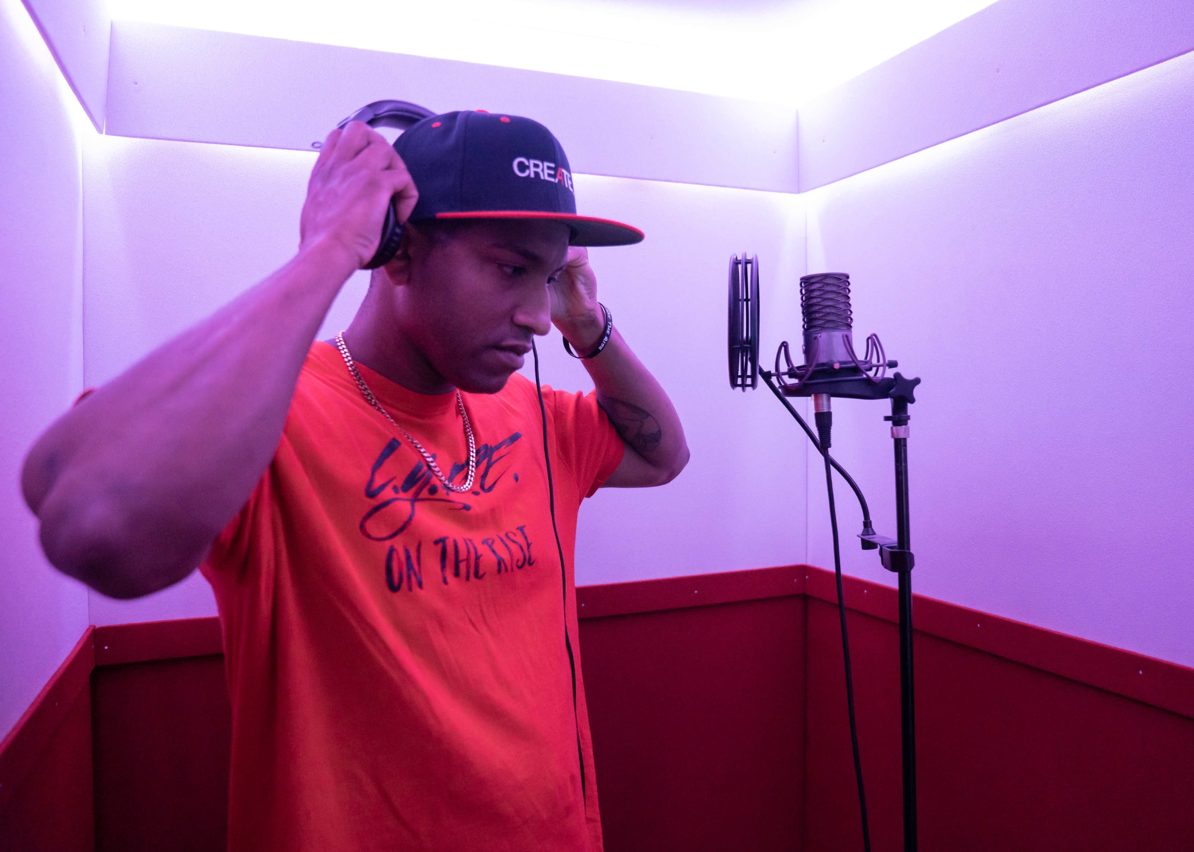 A person wearing a red shirt and a black cap is adjusting headphones in a recording studio.