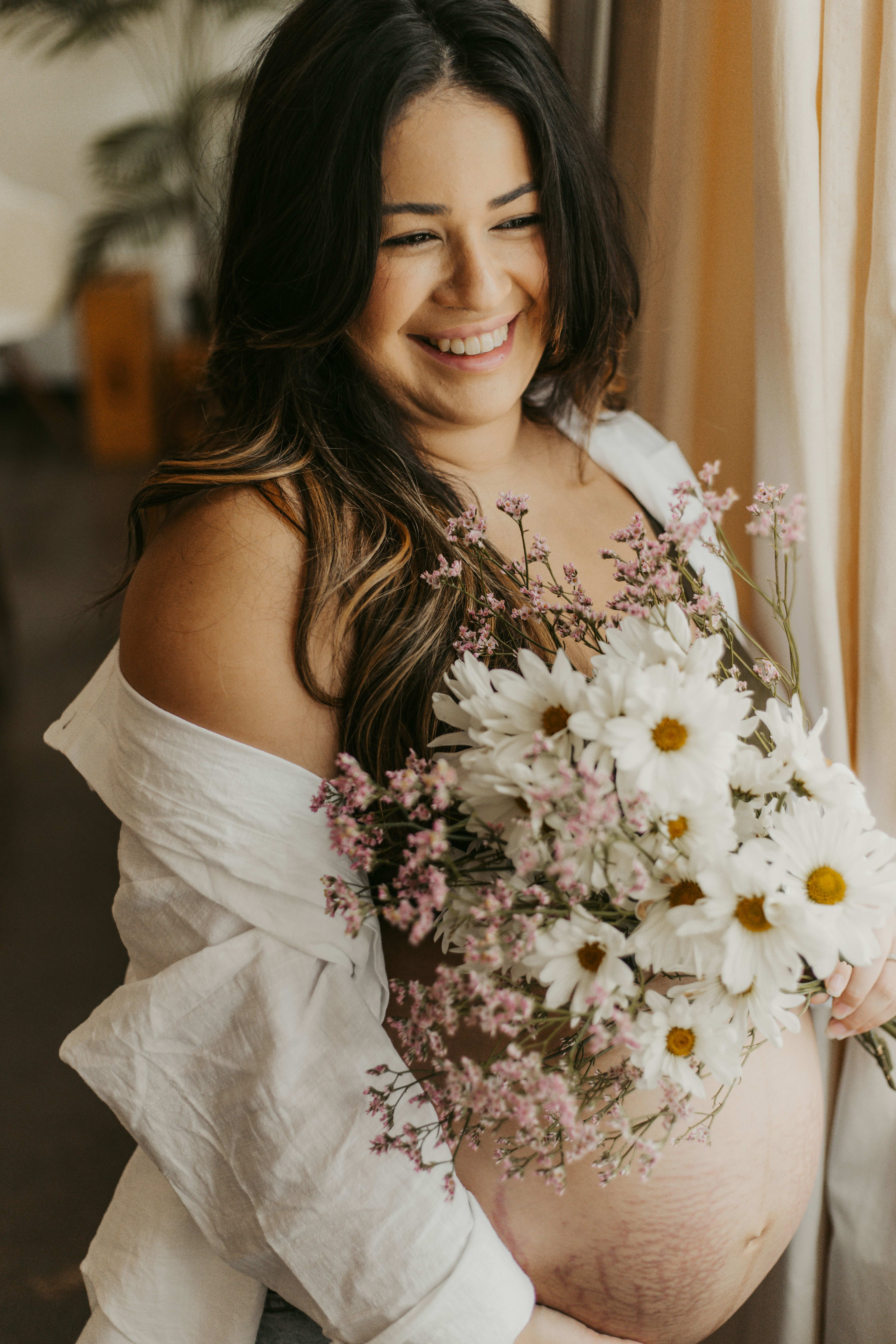 A white maternity photo shoot featuring a pregnant woman holding a bouquet of flowers.