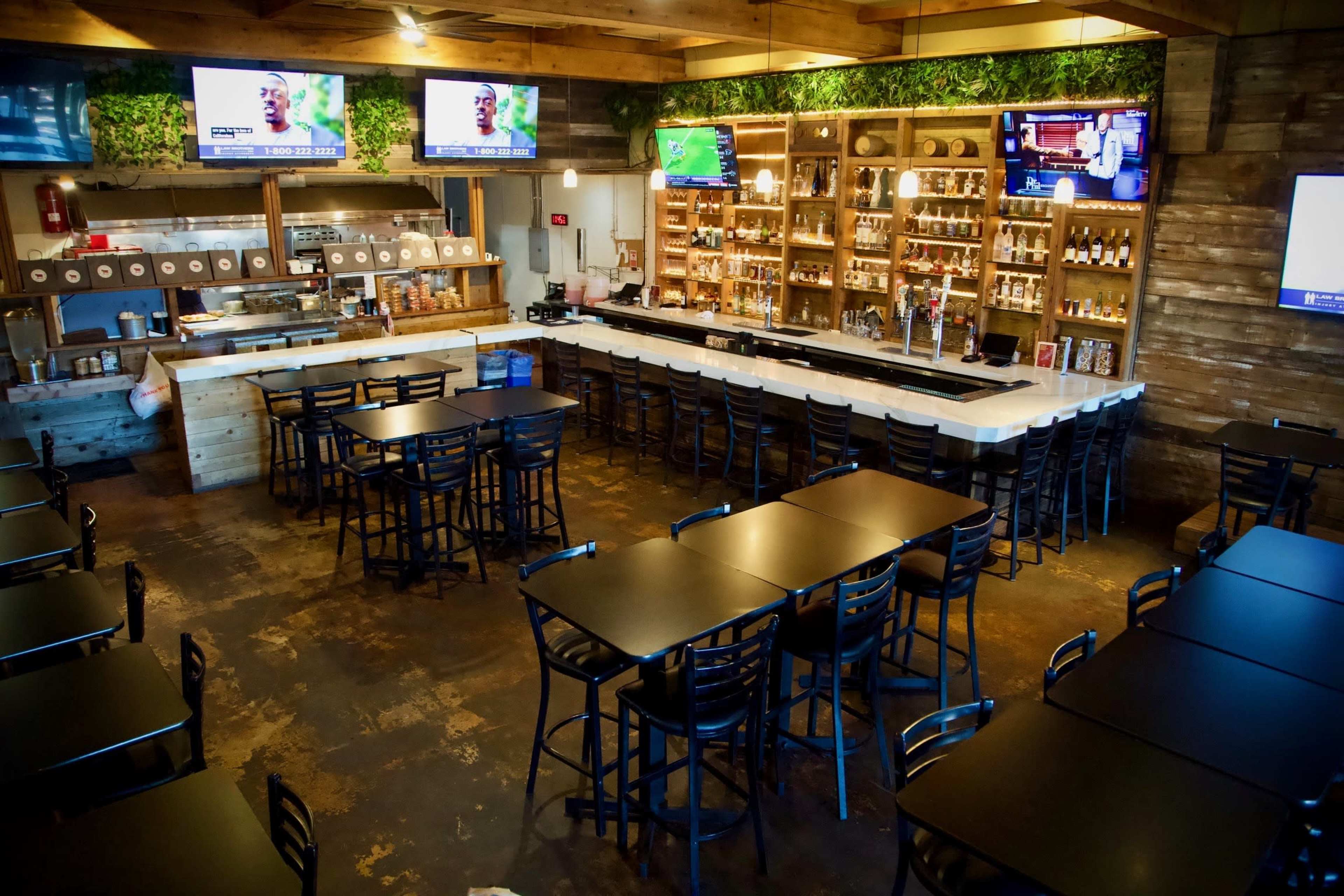 The image shows a spacious bar and dining area with multiple flat-screen TVs, wooden decor, and rows of tables and chairs arranged for patrons.